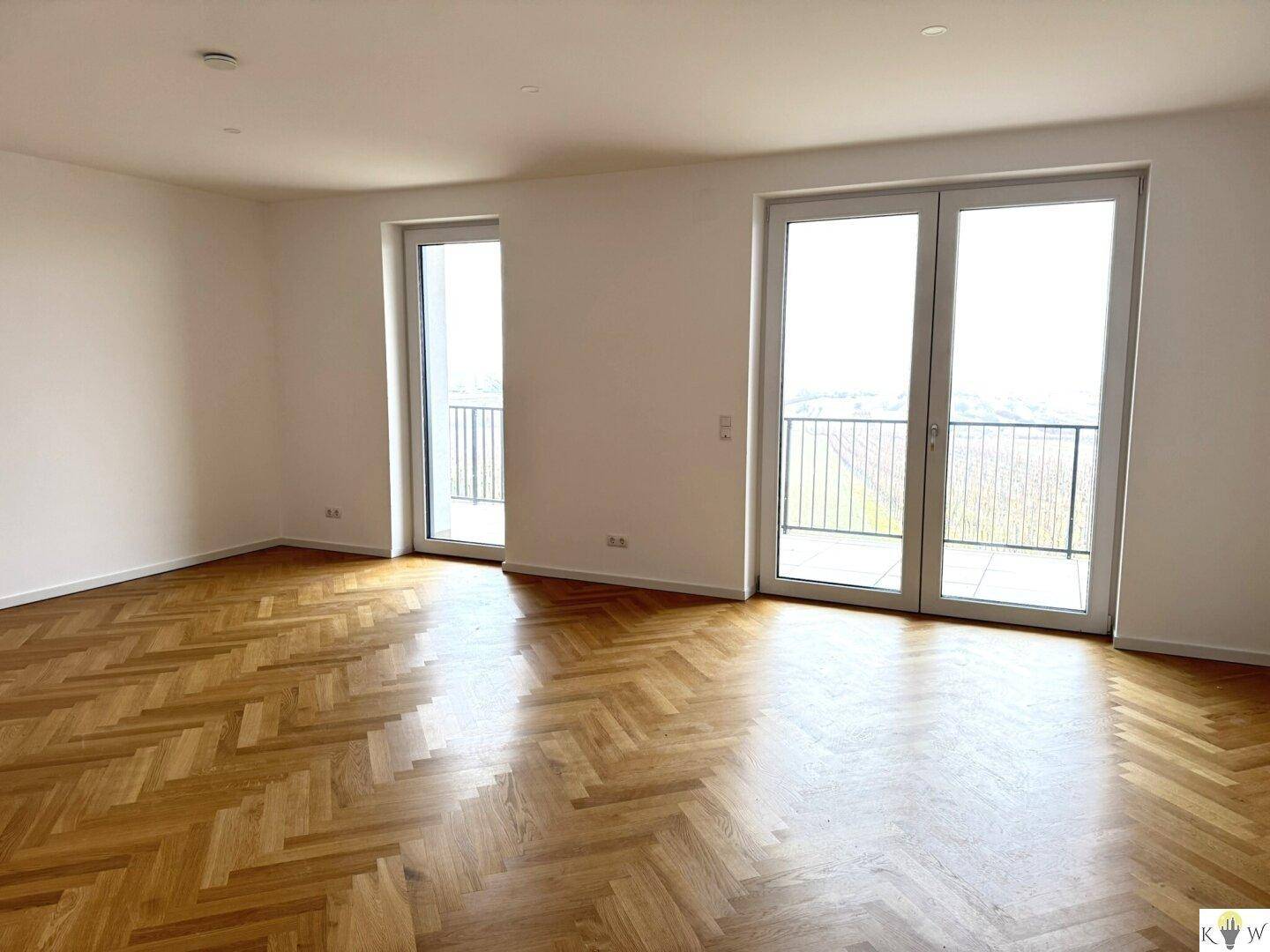 Helles Wohnzimmer mit elegantem Fischgrätparkett und Zugang zu zwei Balkonen mit Weitblick.