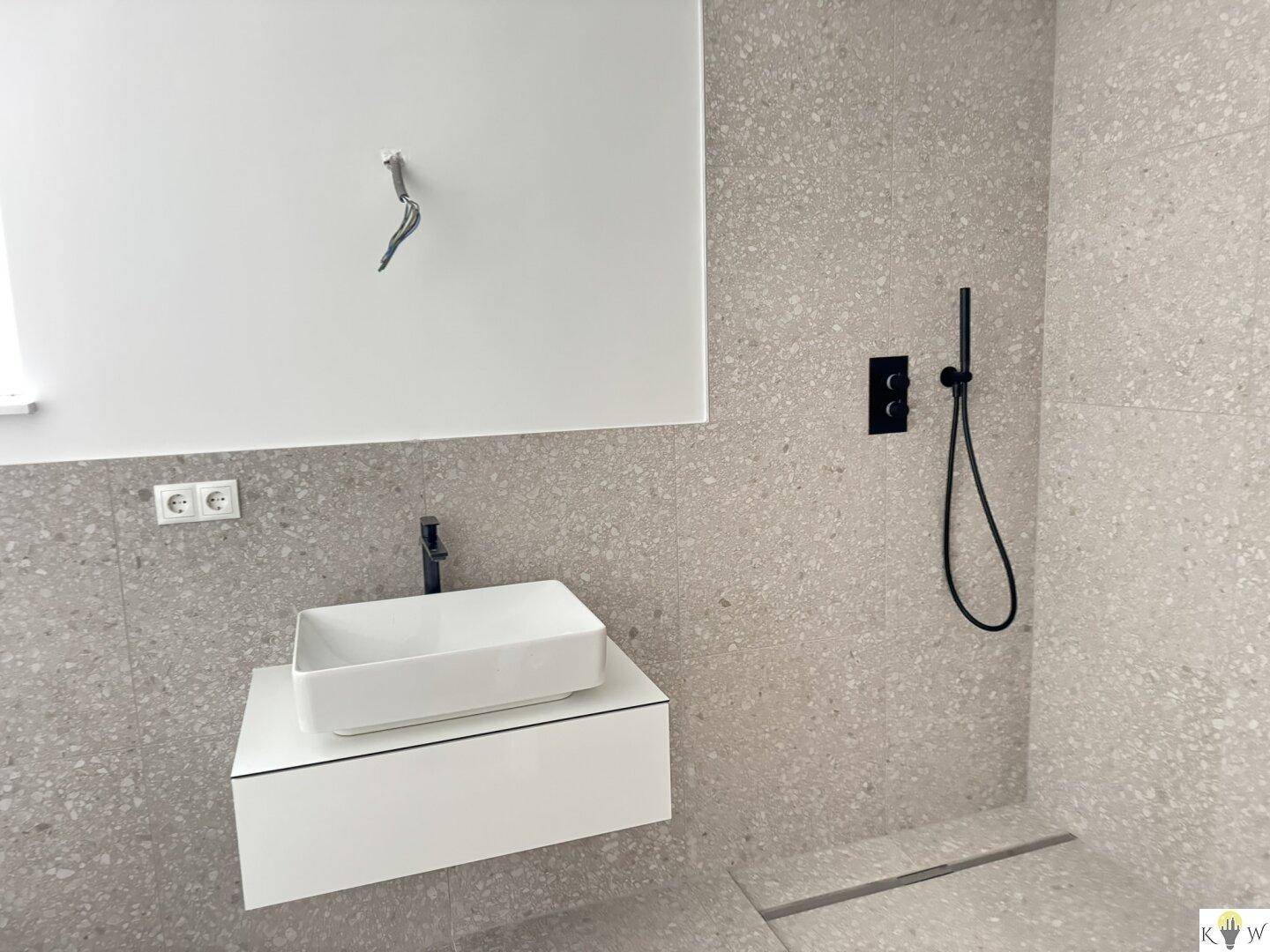 Modernes Badezimmer mit großformatigen grauen Fliesen, stilvollem Aufsatzwaschbecken und ebenerdiger Dusche.