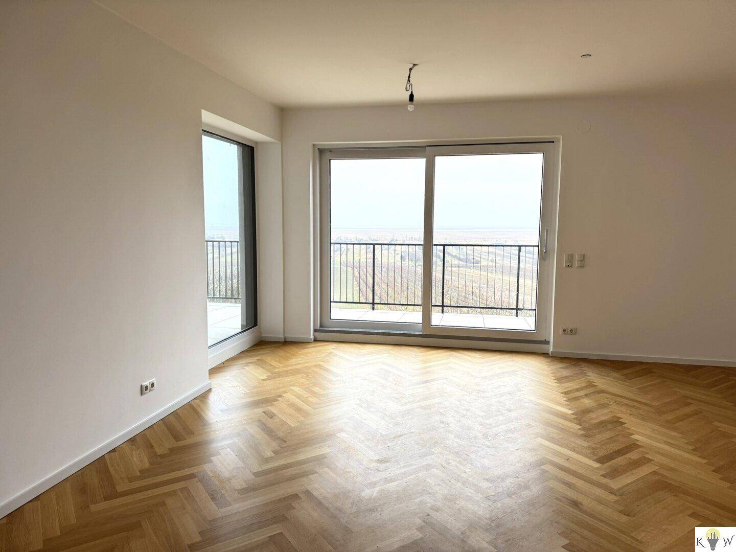 Lichtdurchfluteter Wohnraum mit Fischgrätparkett und weitem Blick ins Grüne vom Balkon.