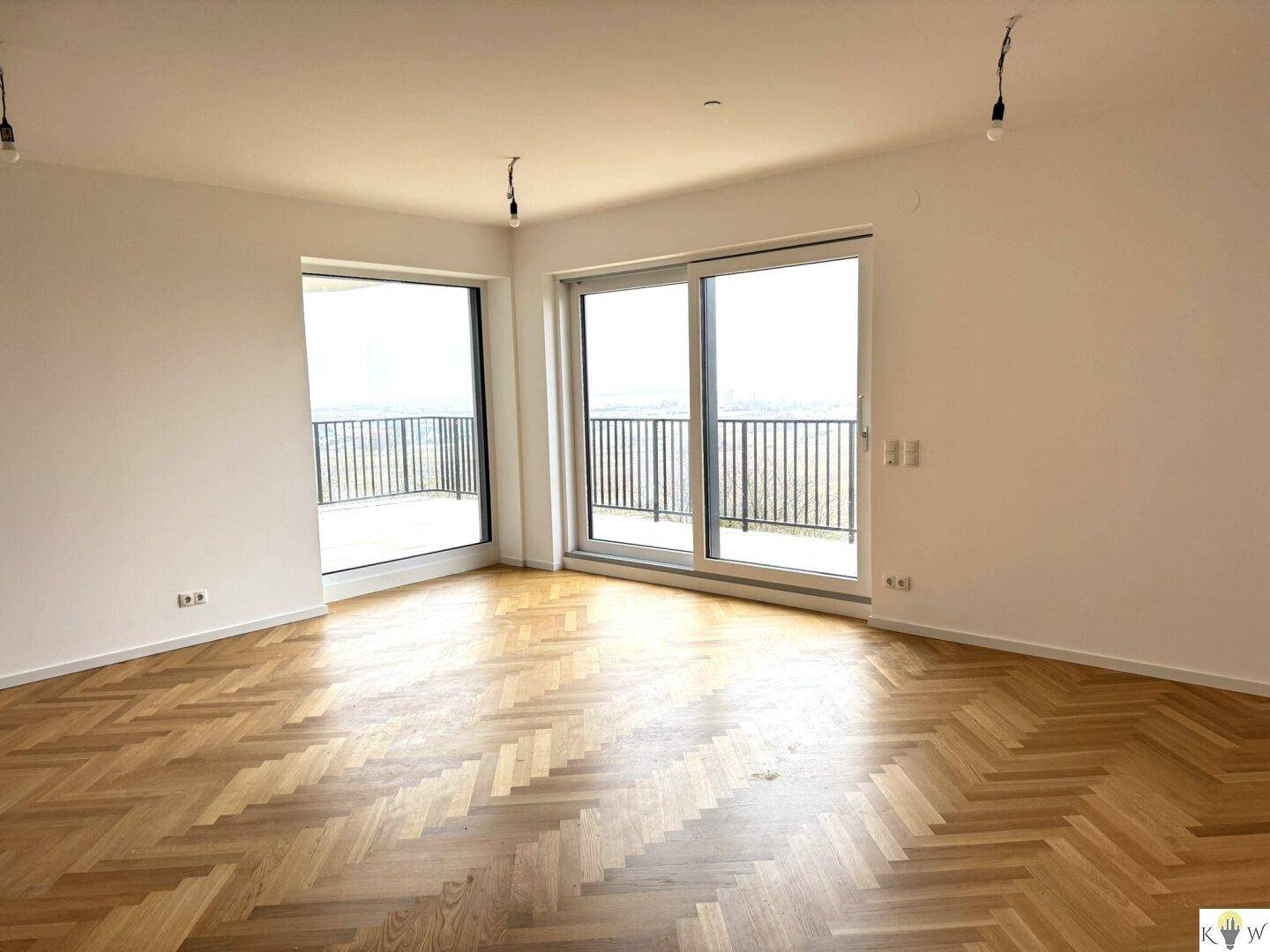 Helles Wohnzimmer mit Fischgrätparkett und großen Schiebetüren zum Balkon mit Weitblick.