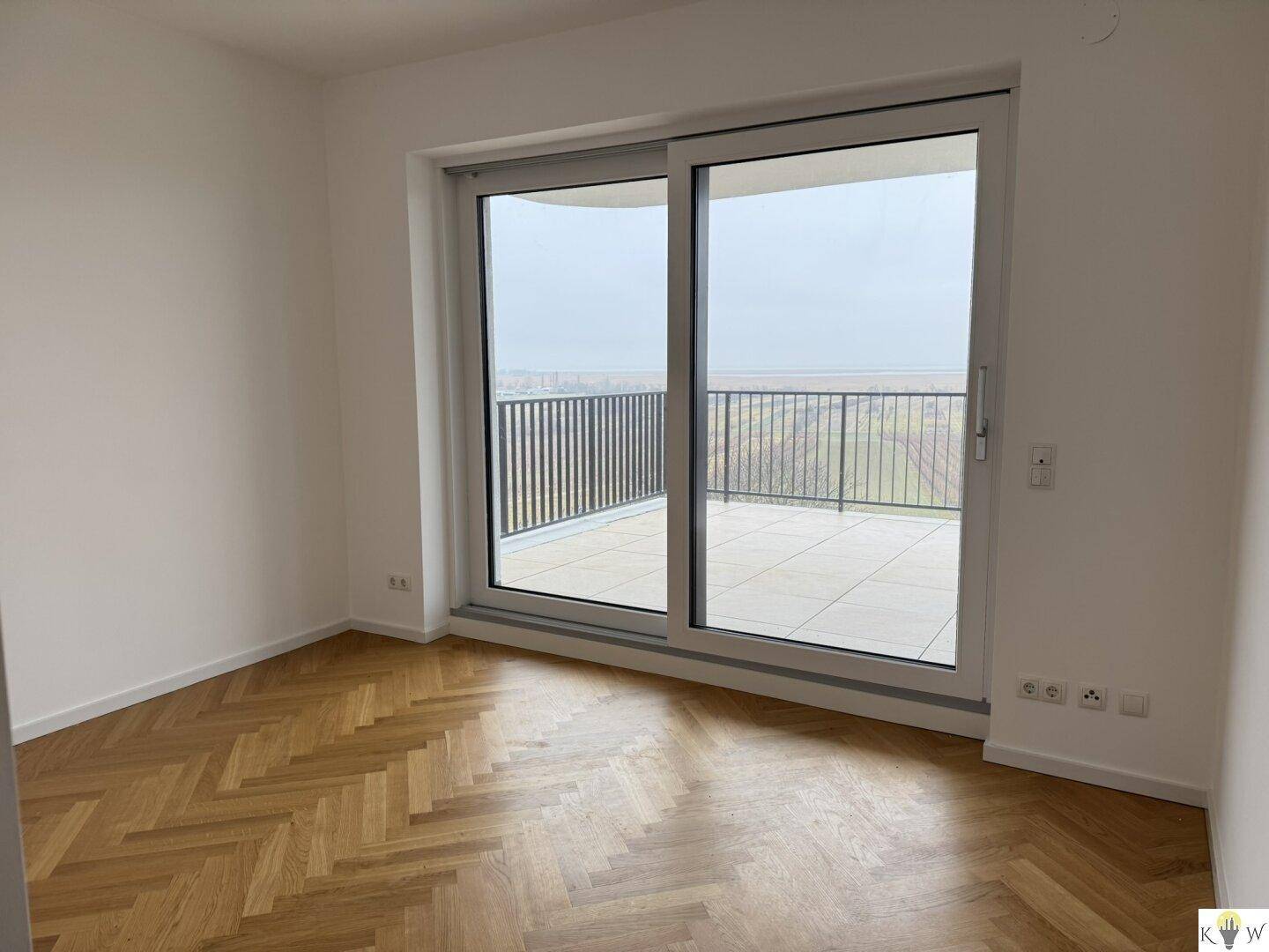 Helles Zimmer mit Parkettboden und großem Fenster mit Zugang zum Balkon und Weitblick.