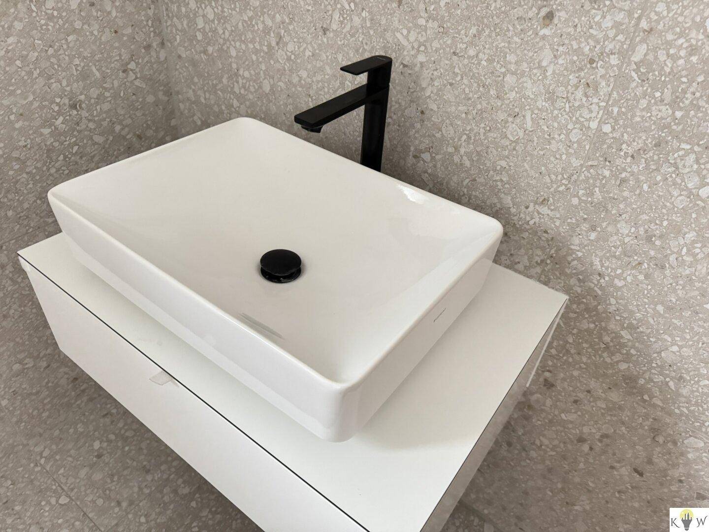 Modernes Waschbecken mit schwarzer Armatur auf einem weißen Unterschrank im Badezimmer.