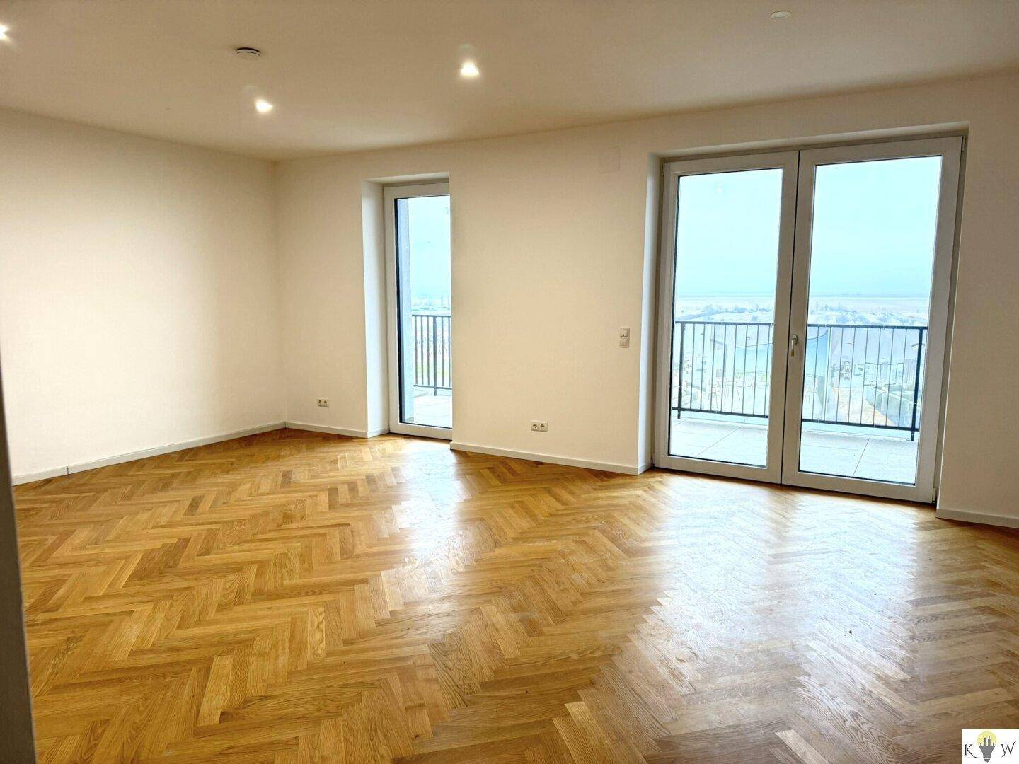 Heller Wohnraum mit elegantem Fischgrätparkett und Zugang zu zwei Balkonen mit Weitblick.