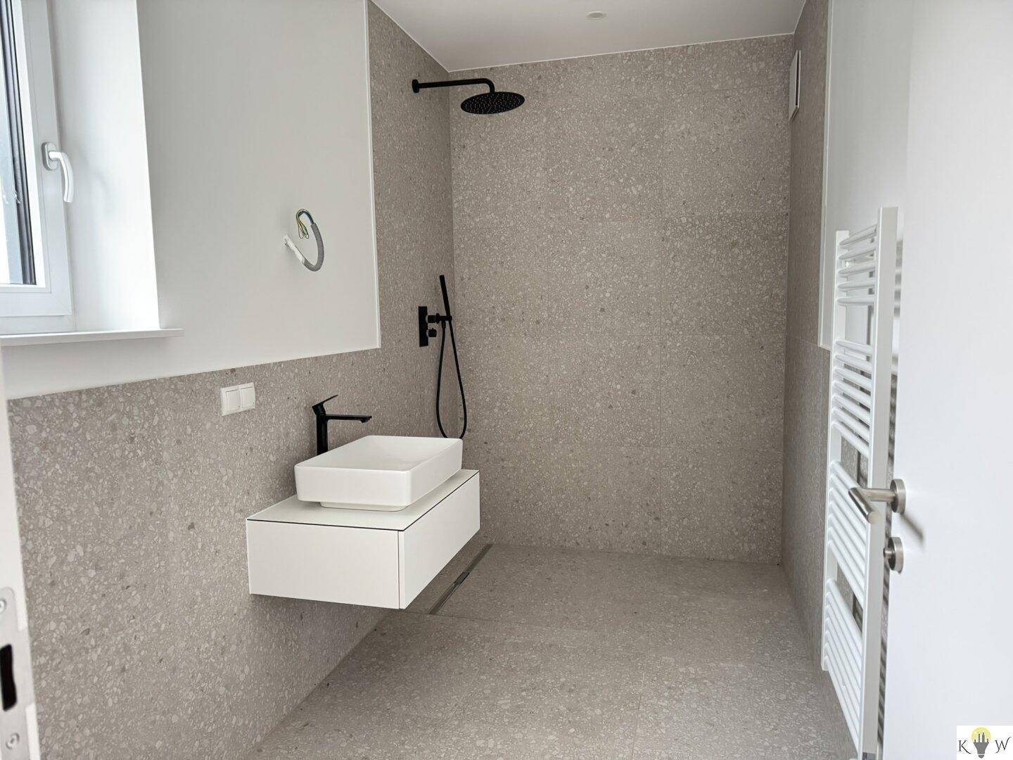 Modernes Badezimmer mit ebenerdiger Dusche, schwebendem Waschtisch und grauem Fliesenboden.