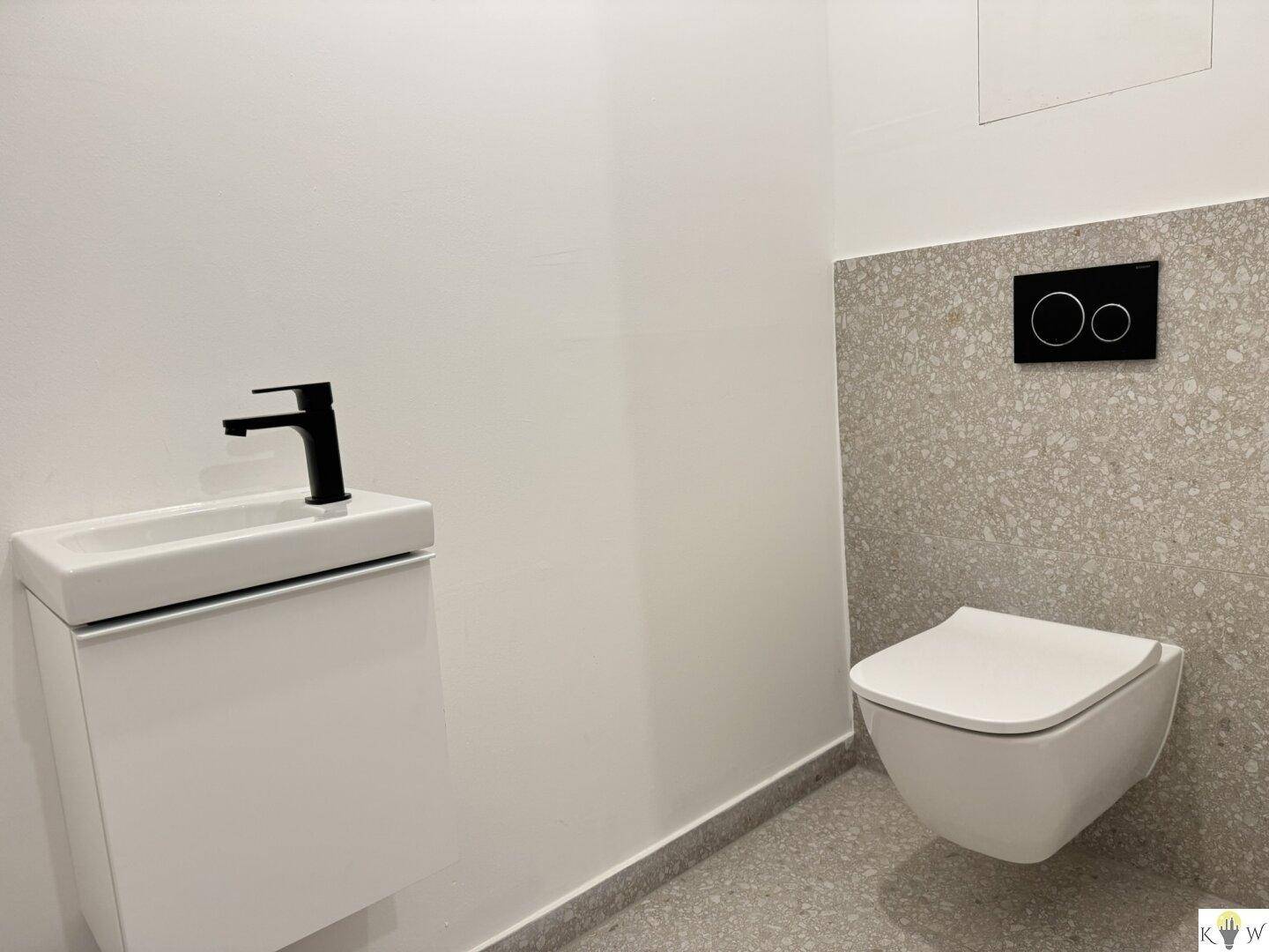 Gäste-WC mit wandhängender Toilette, kleinem Waschtisch und modernen grauen Fliesen.