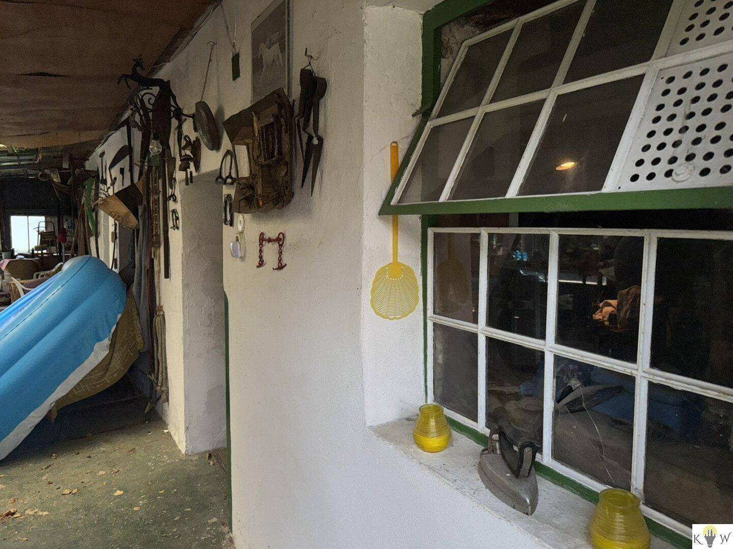 Rustikaler Abstellraum mit altem Fenster, Werkzeugen an der Wand und einem aufblasbaren Boot.