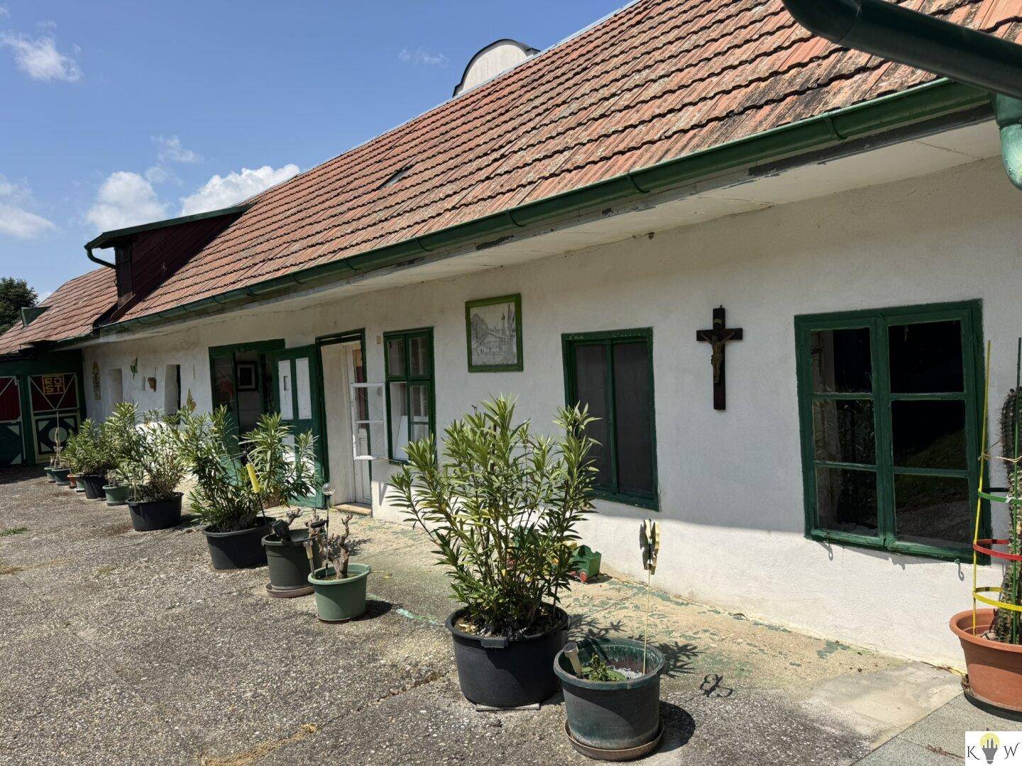 Traditionelle Hausfassade mit grünen Fensterrahmen, Topfpflanzen und einem religiösen Kreuz an der Wand.