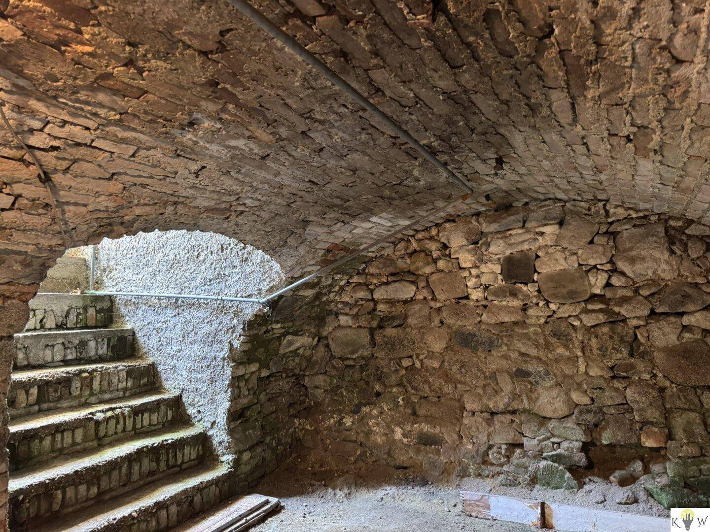 Historischer Kellerraum mit freiliegenden Steinmauern, Ziegelgewölbedecke und Steintreppe.