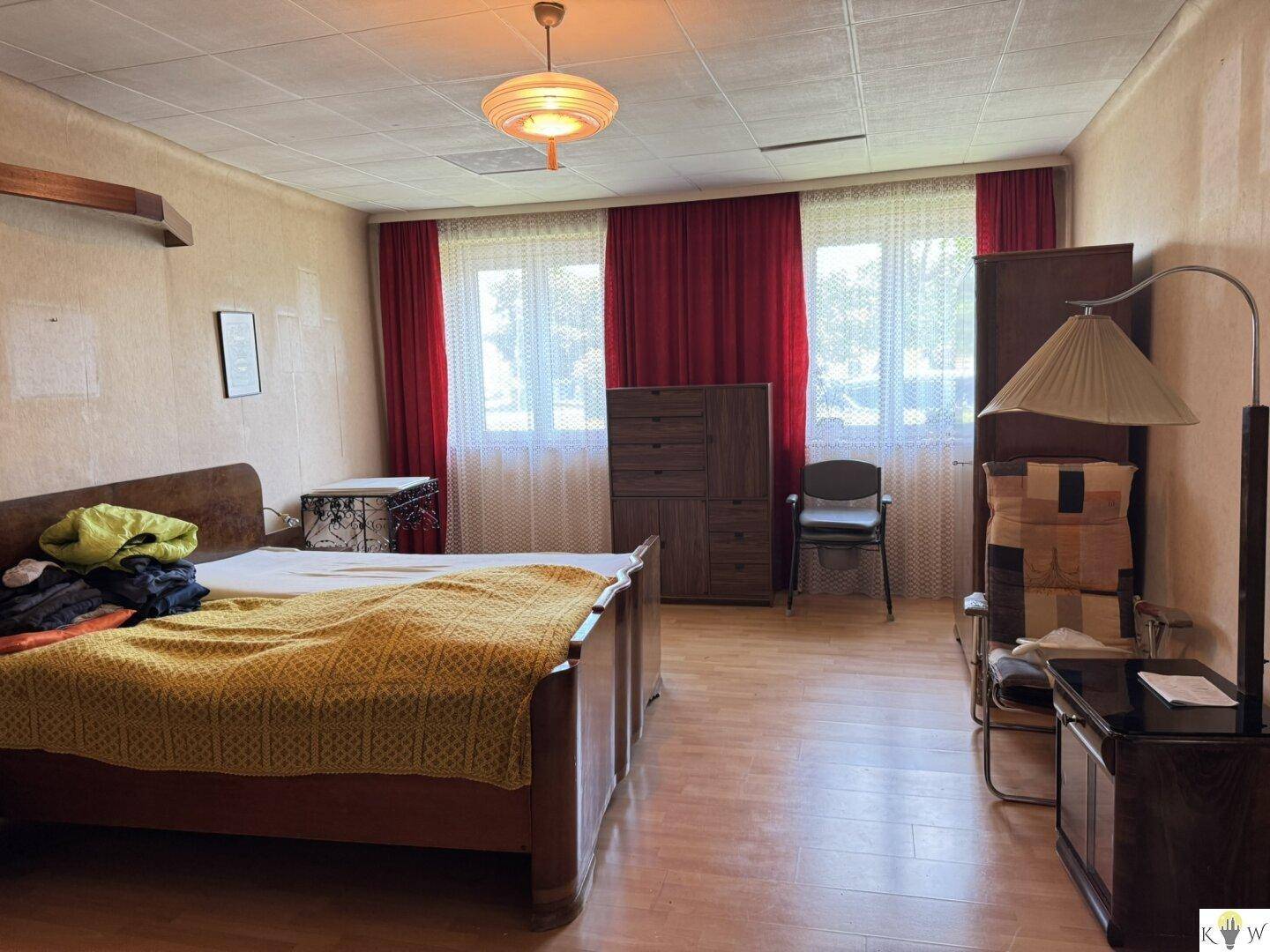 Geräumiges Schlafzimmer mit Doppelbett, Holzmöbeln, roten Vorhängen und Laminatboden.