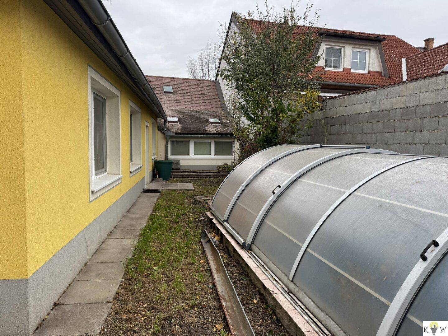 Seitenansicht des Hauses mit einem Gewächshaus und einem schmalen Rasenstreifen.