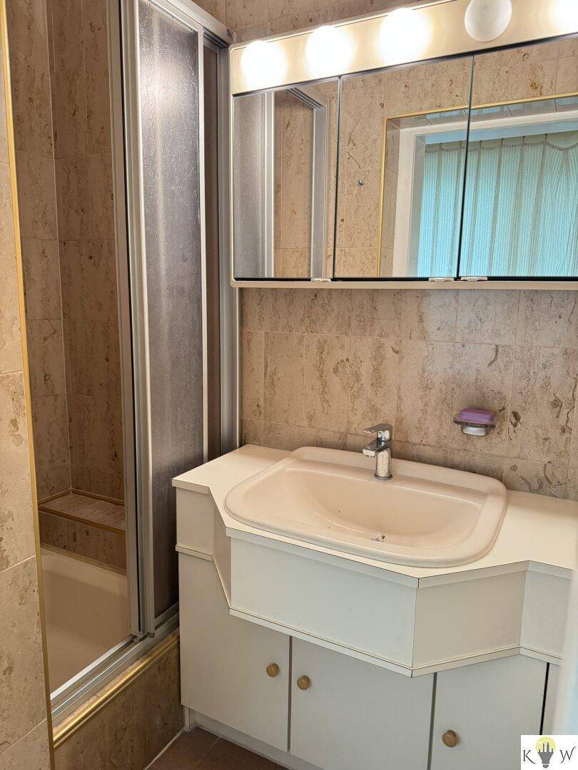 Badezimmer mit beigefarbenen Fliesen, Waschtisch und Duschkabine.