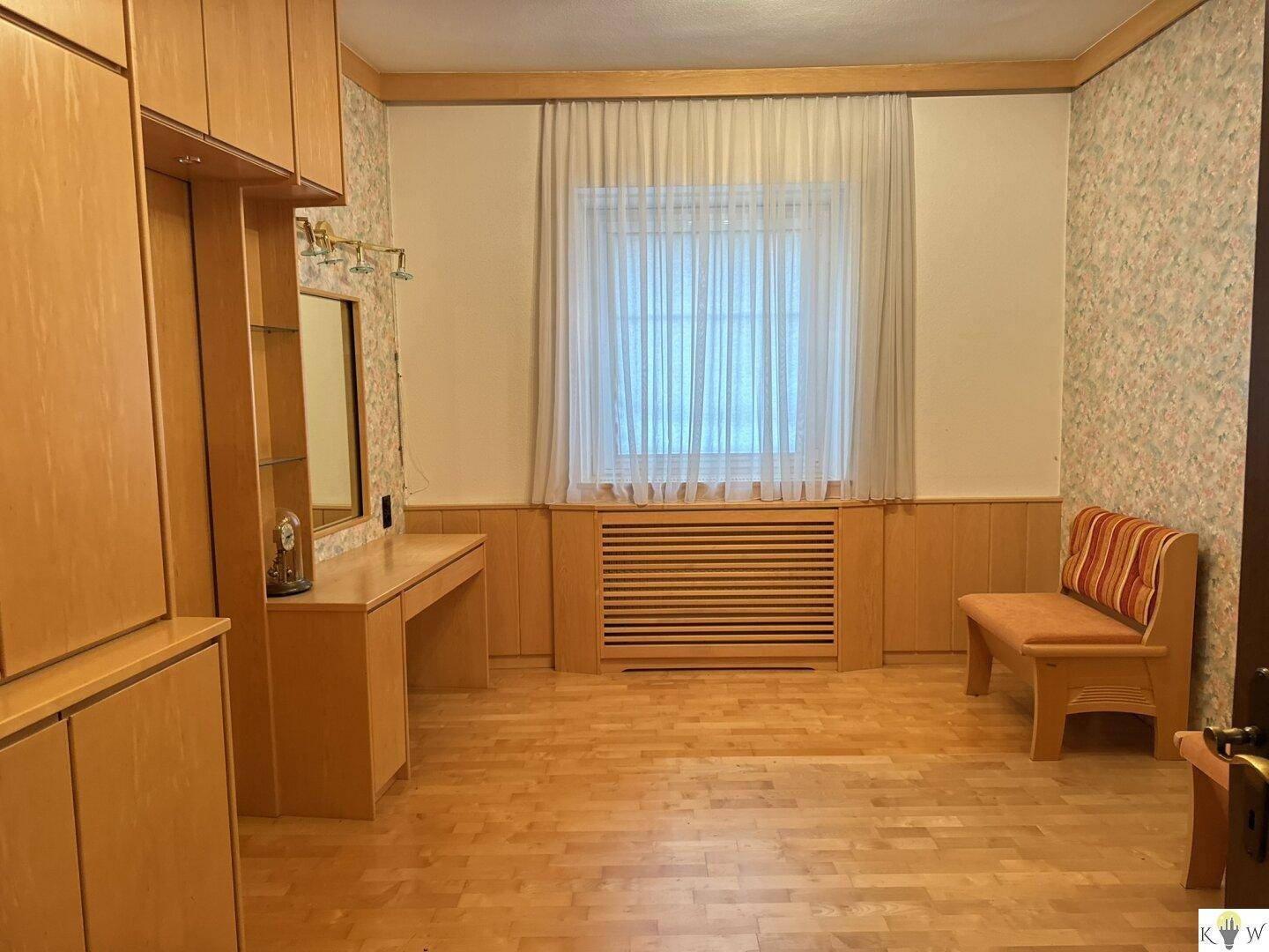 Schlafzimmer mit Holzparkett, Einbauschränken und einem Fenster mit Vorhängen.