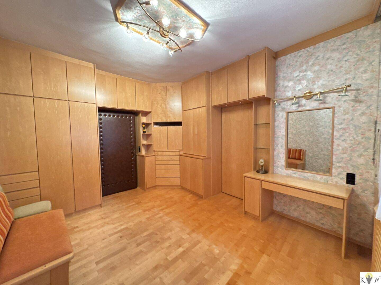Schlafzimmer mit umfangreichen Einbauschränken aus hellem Holz und Parkettboden.