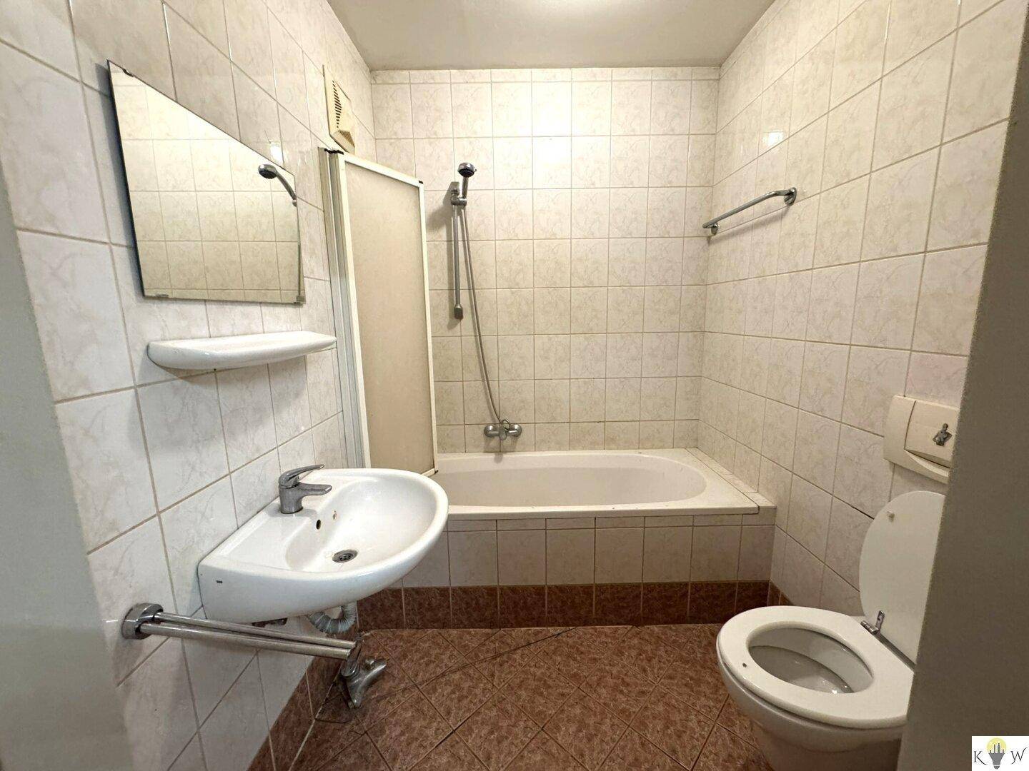 Funktionales Badezimmer mit Badewanne, Toilette und Waschbecken, komplett gefliest in hellen Farbtönen.