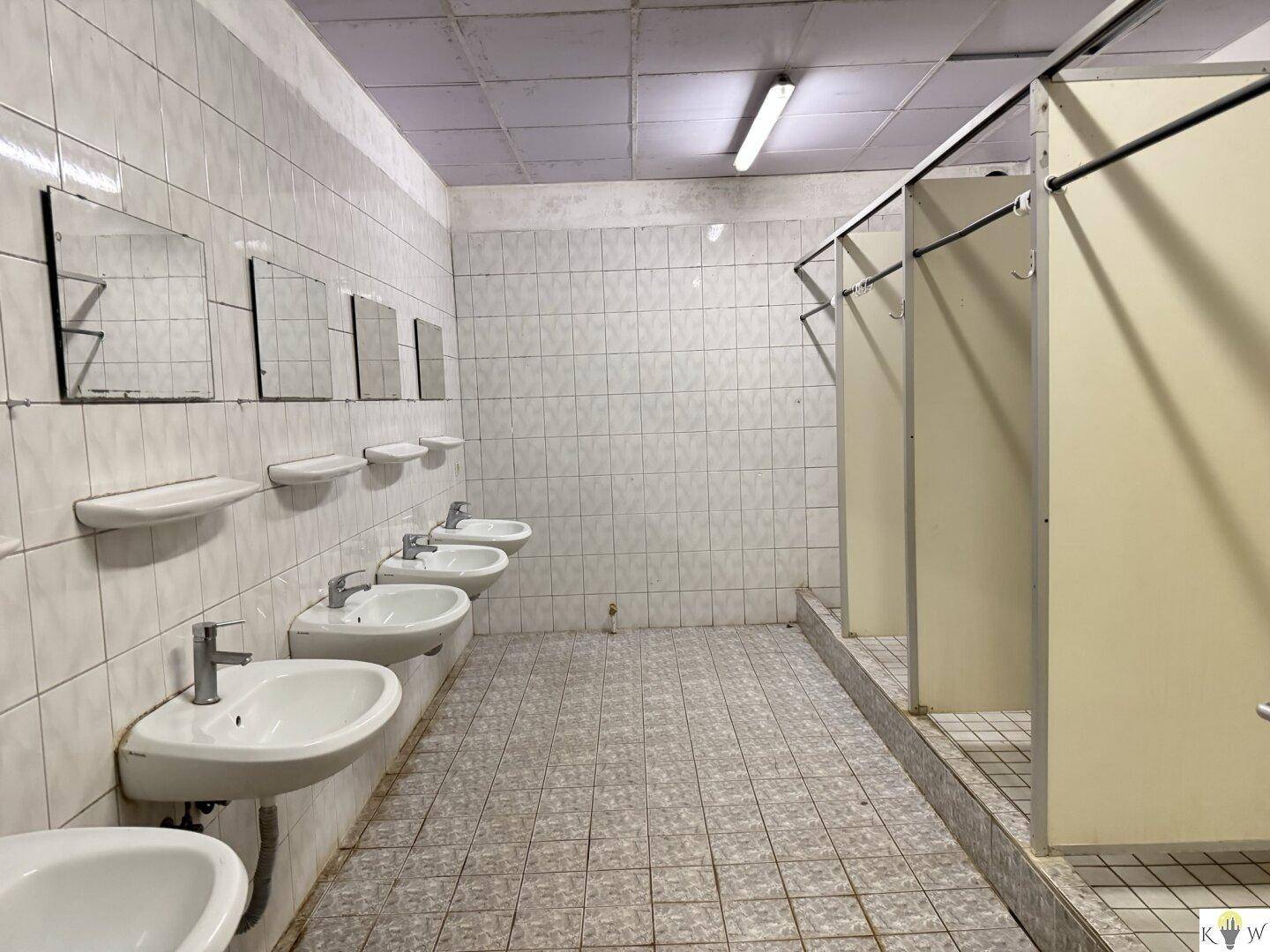 Großer Waschraum mit mehreren Waschbecken und Duschkabinen, vollständig gefliest und funktional.
