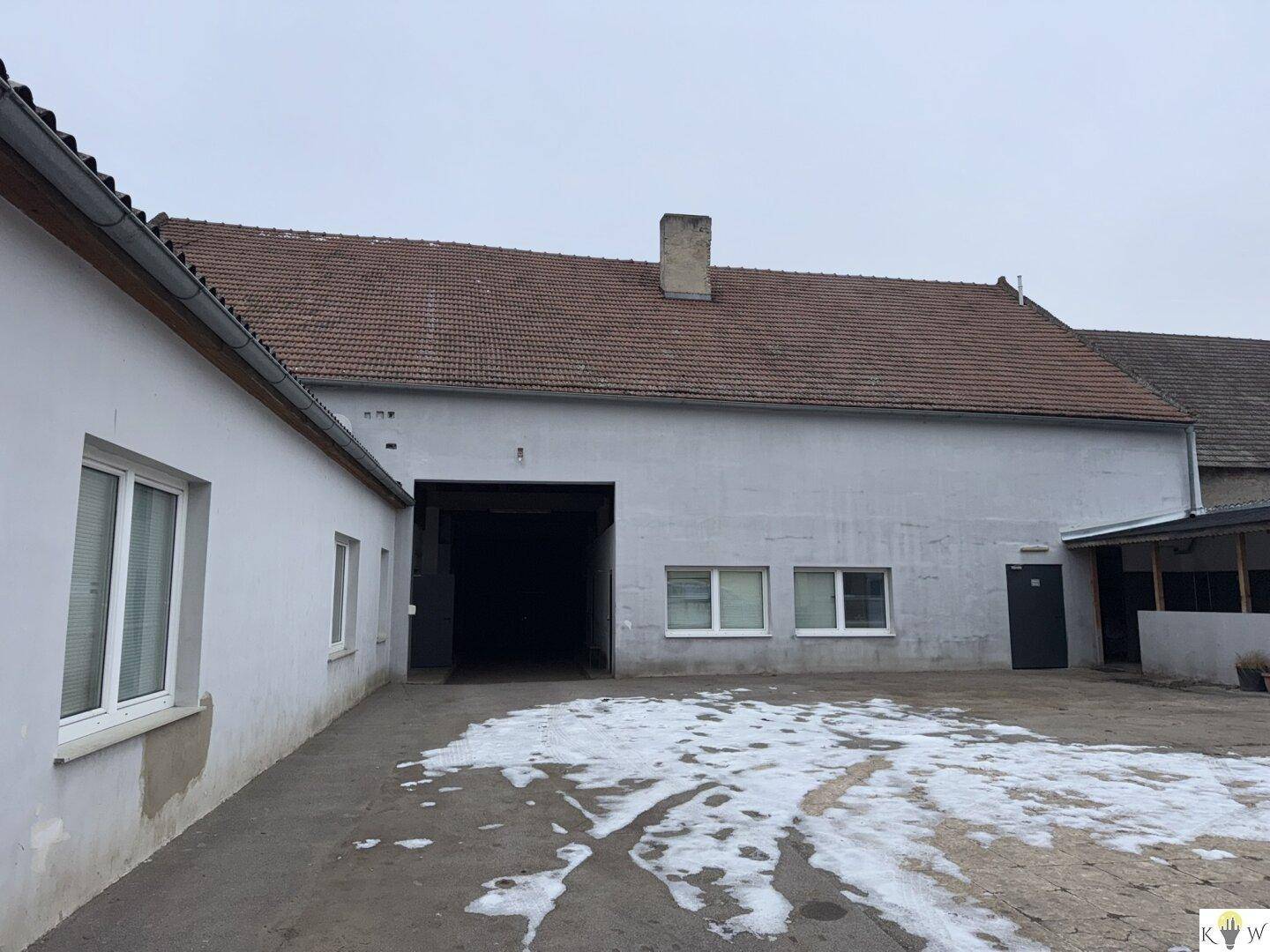 Hinterhofbereich mit einem großen Tor, einem Nebengebäude und Schneeresten auf dem Boden.