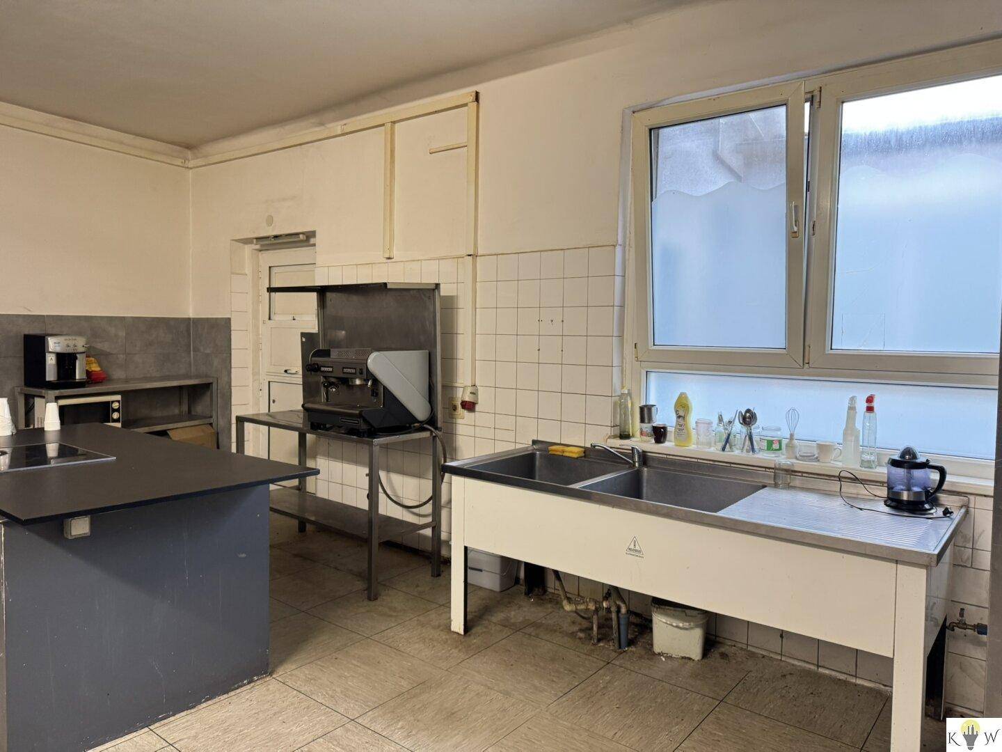 Funktionale Küche mit Doppelspülbecken, Fliesenwänden und einem Fenster, das Tageslicht hereinlässt.