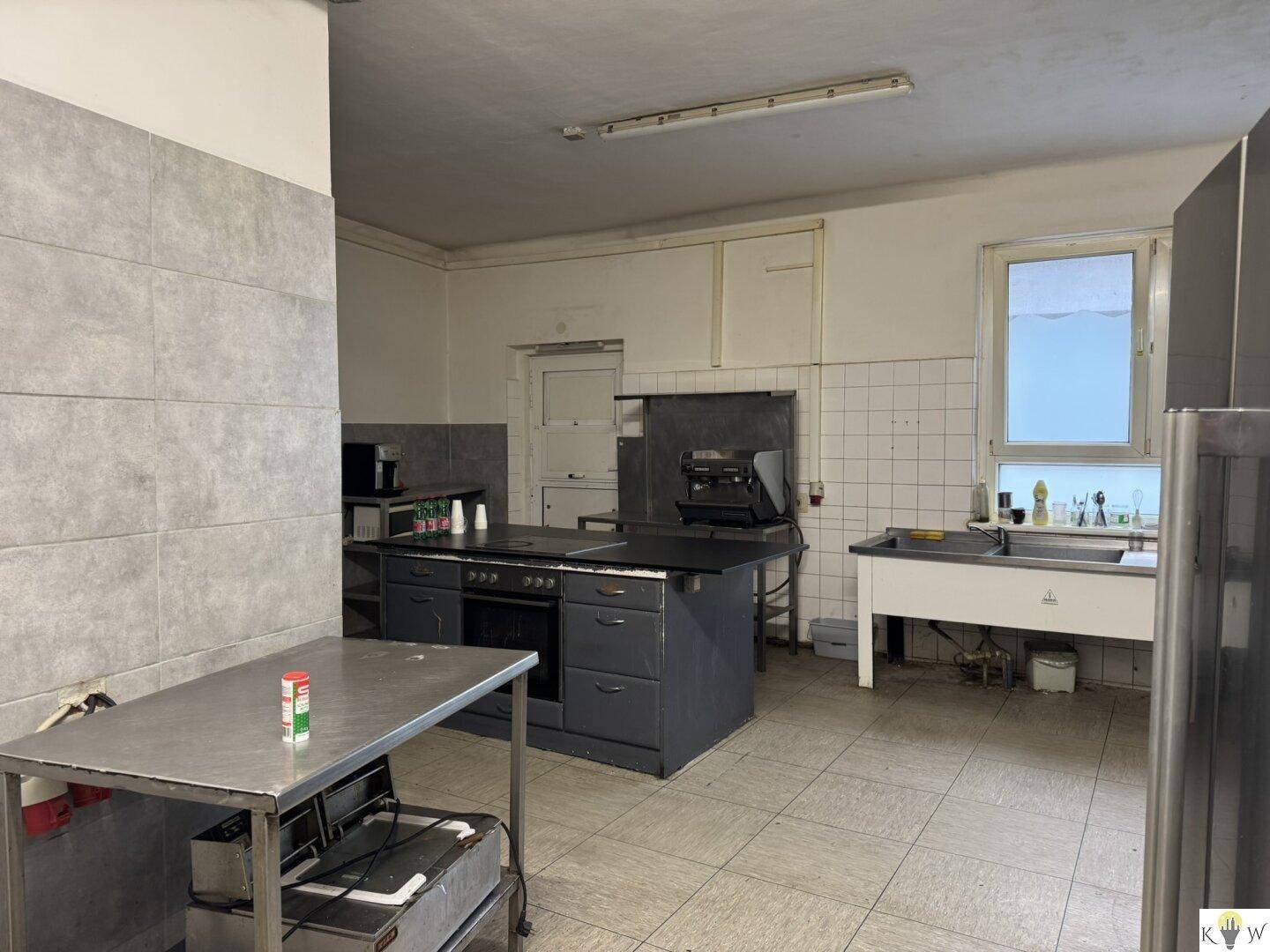 Geräumige Industrieküche mit Kochinsel, Edelstahlflächen und Fliesenboden, ideal für die Zubereitung von Speisen.