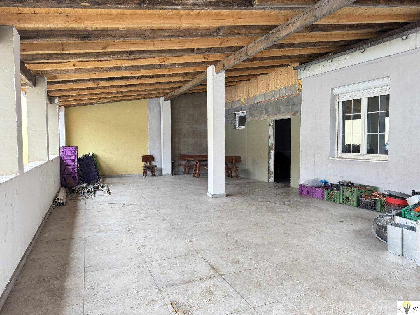 Überdachte Terrasse mit Fliesenboden und sichtbaren Holzbalken, ideal für einen geschützten Außenbereich.