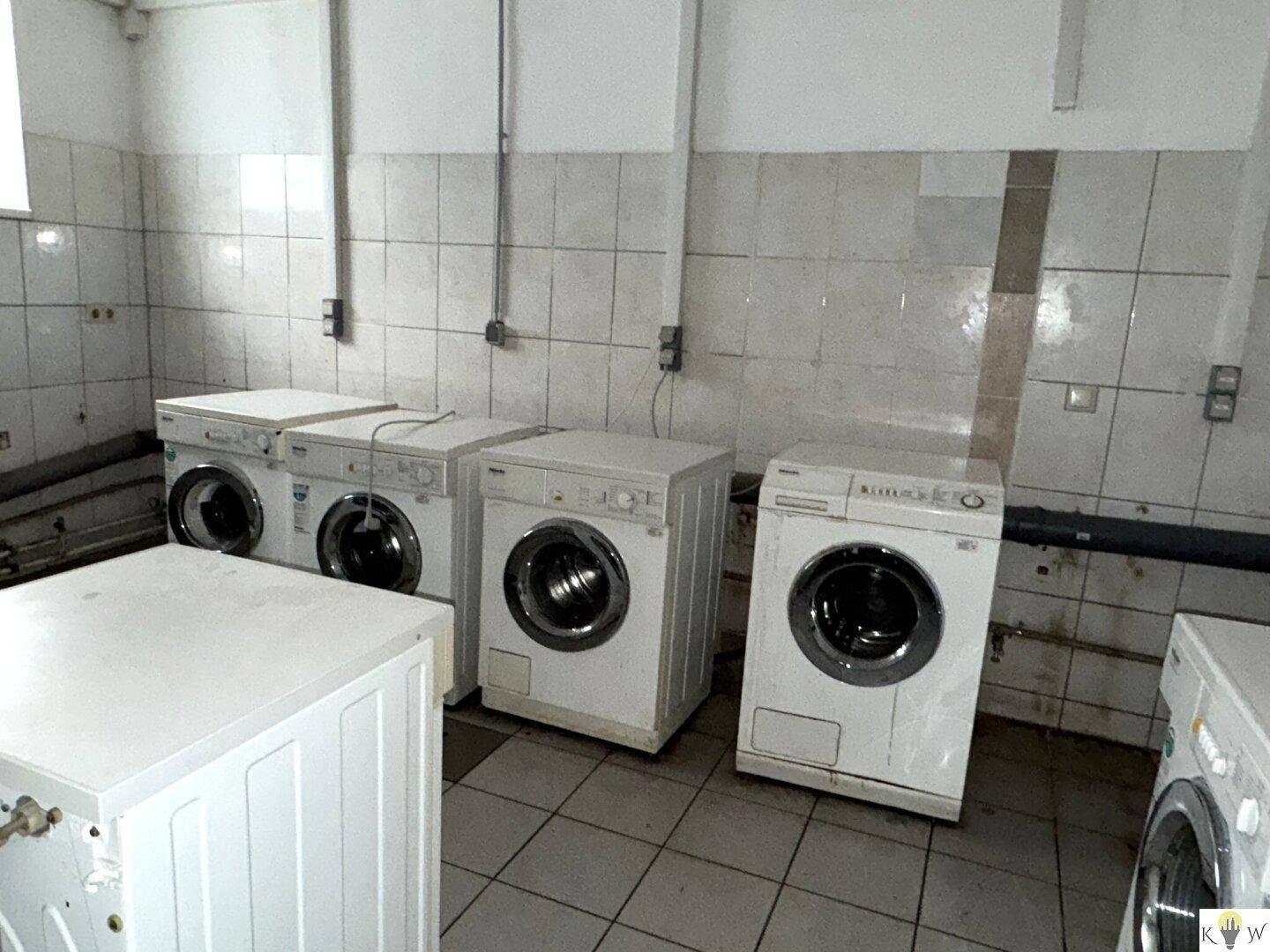 Waschküche mit mehreren Waschmaschinen und Fliesenboden, bereit für den Wäscheservice.
