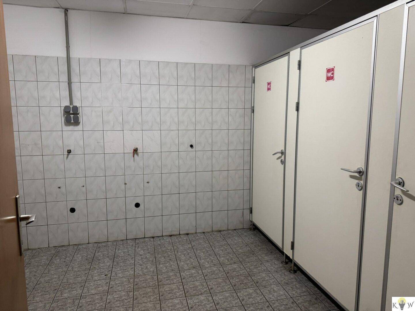 Reihen von Toilettenkabinen in einem gefliesten Raum, sauber und funktional für mehrere Nutzer.