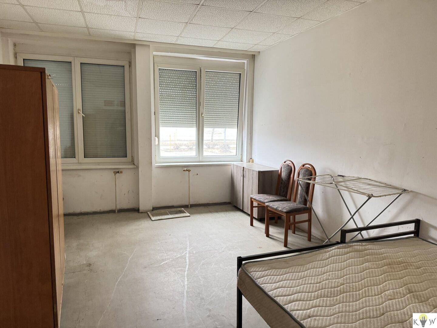 Einfaches Schlafzimmer mit zwei Betten, einem Kleiderschrank und einem Fenster mit Rollladen.