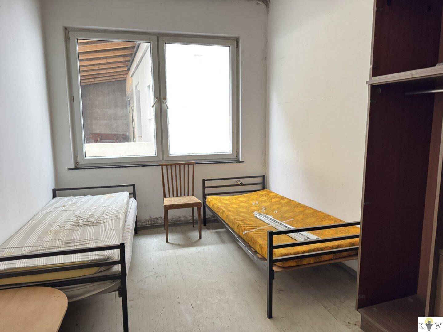 Einfaches Schlafzimmer mit zwei Einzelbetten und einem Fenster, das den Blick auf einen überdachten Bereich freigibt.