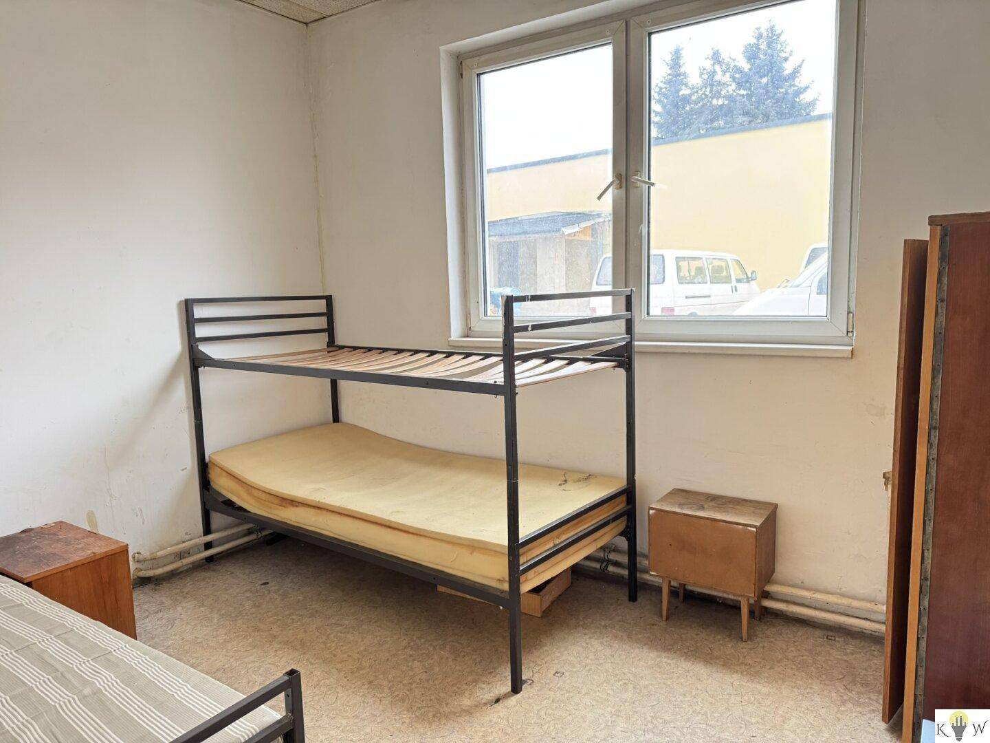 Schlichtes Schlafzimmer mit einem Etagenbett und einem Einzelbett, ergänzt durch einen Nachttisch und ein Fenster.