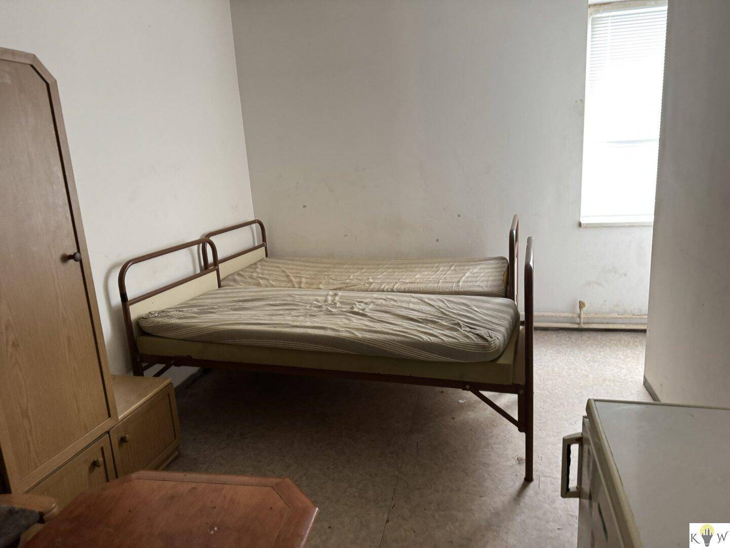 Einfaches Schlafzimmer mit zwei Einzelbetten, einem Kleiderschrank und einem Fenster mit Blick nach draußen.