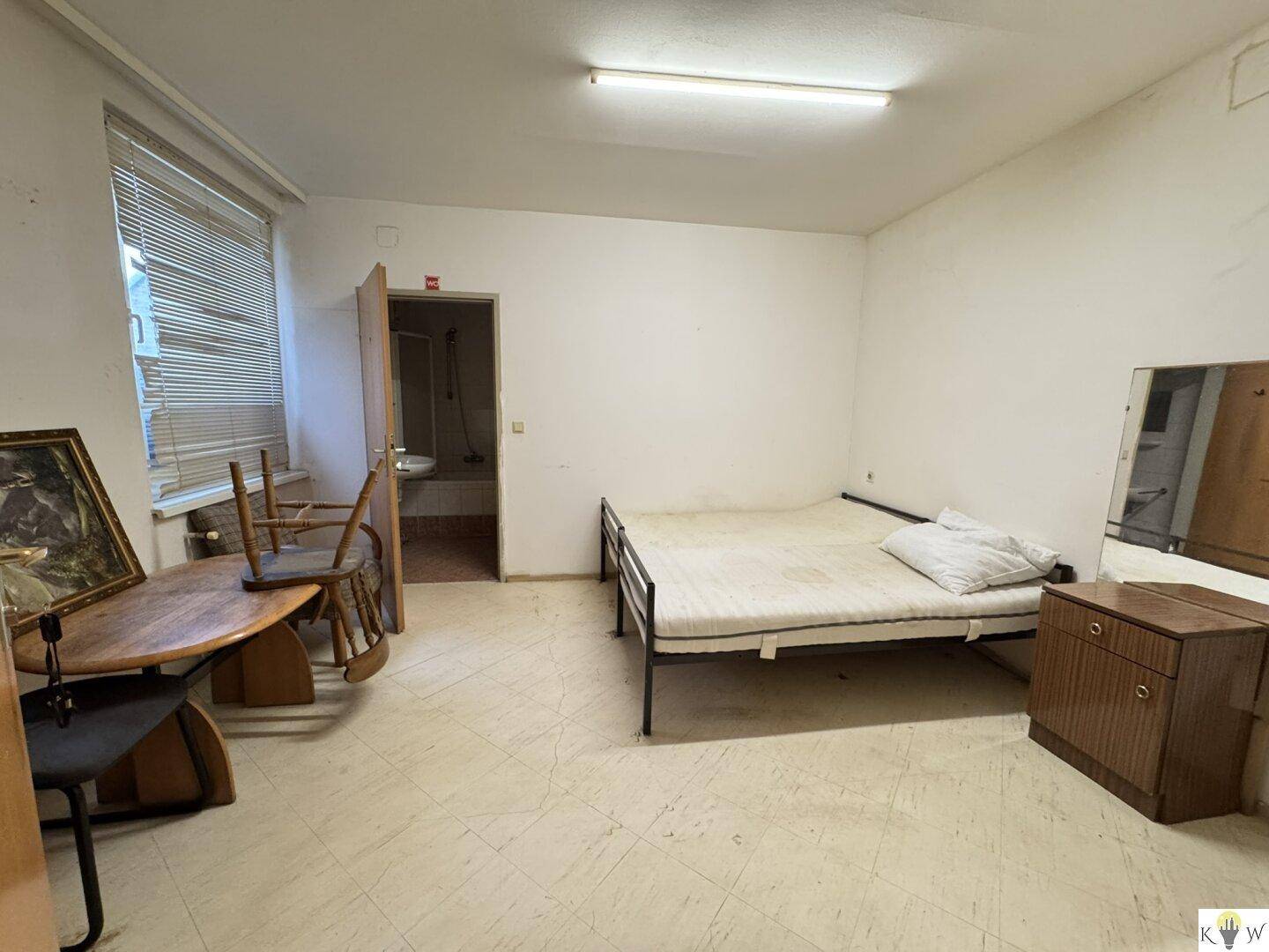 Einfaches Schlafzimmer mit einem Bett, einem Tisch und einem offenen Zugang zu einem Badezimmer.