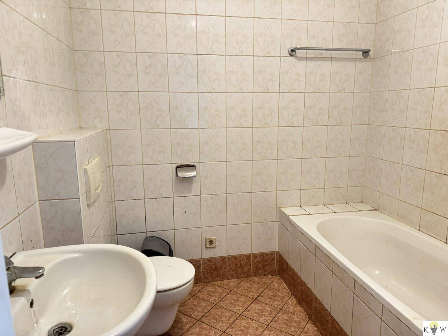 Einfaches Badezimmer mit Badewanne, Toilette und Waschbecken, vollständig gefliest in hellen Mustern.