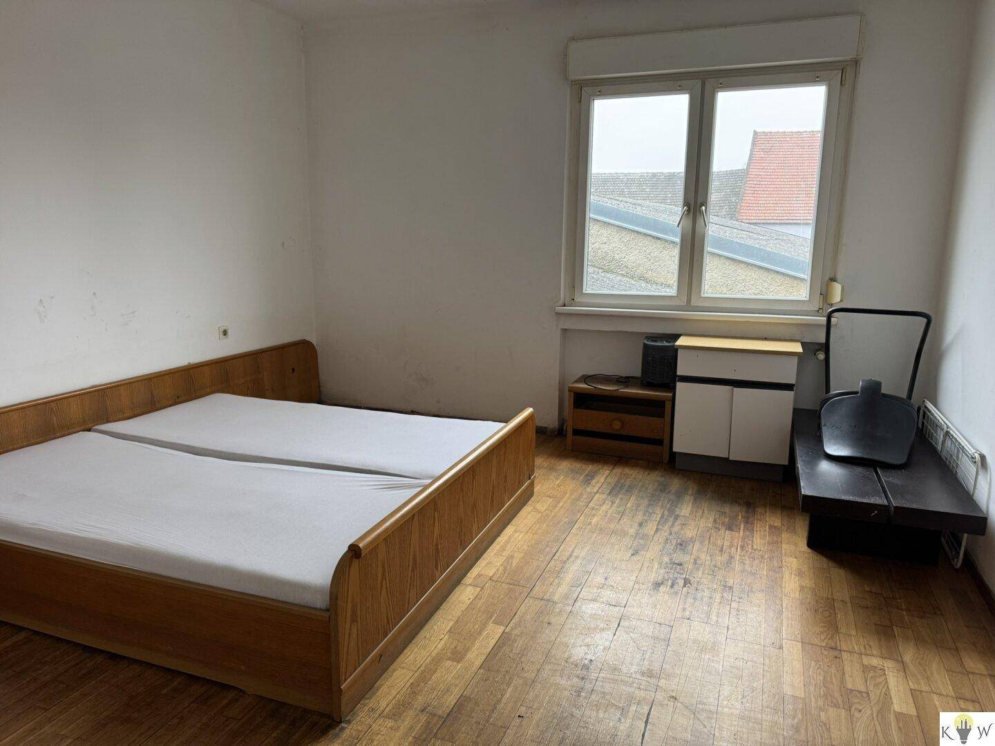 Schlafzimmer mit Doppelbett und Holzboden, beleuchtet durch ein Fenster mit Blick auf die Dächer.