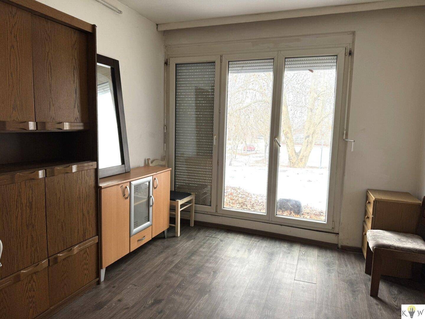 Schlafzimmer mit großem Fenster, das viel Licht hereinlässt, und einem Kleiderschrank aus Holz.