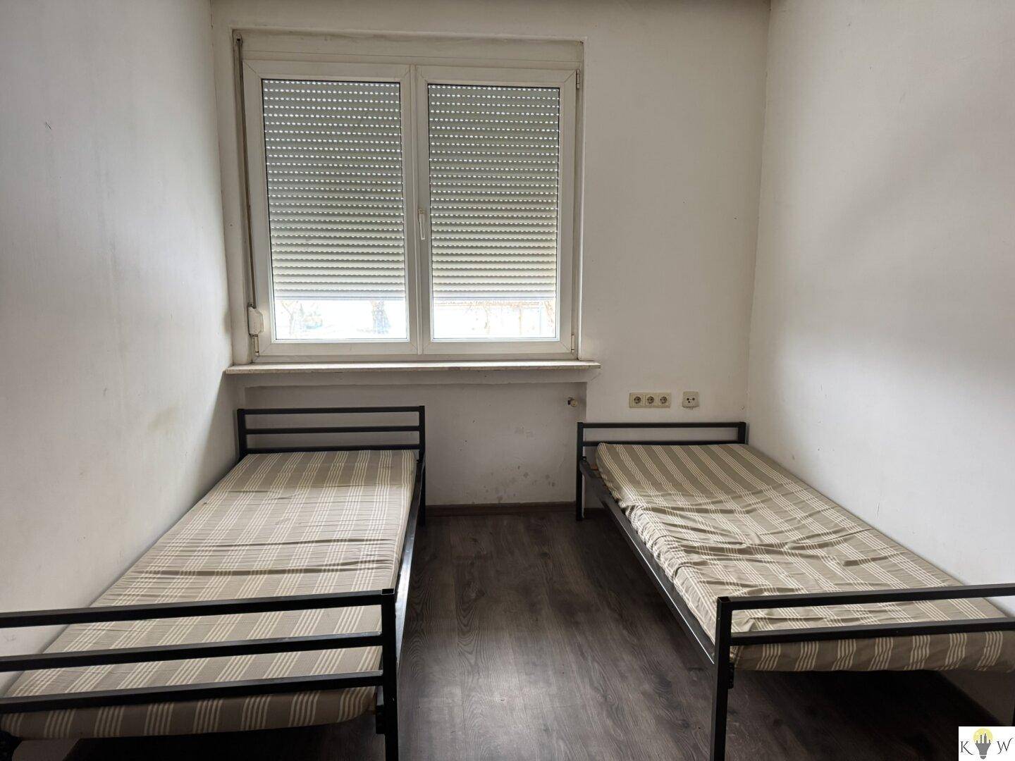 Einfaches Schlafzimmer mit zwei Einzelbetten und einem Fenster mit Rollladen, ausgestattet mit Laminatboden.