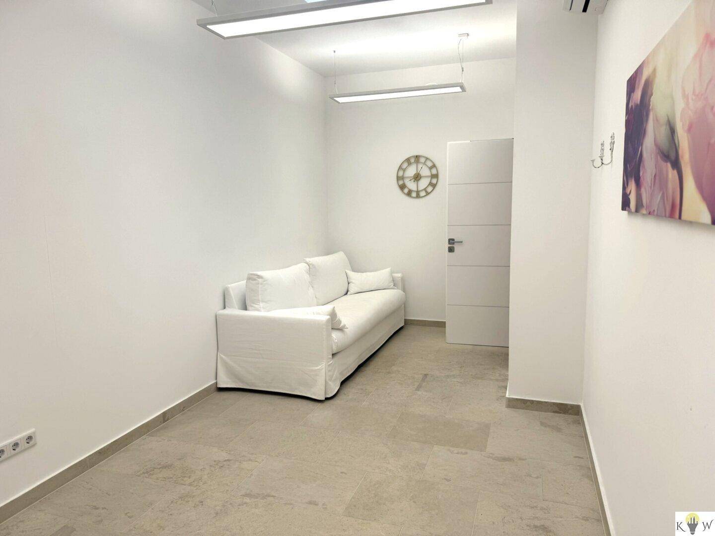 Geräumiger Behandlungsraum mit weißem Sofa, Fliesenboden und Deckenbeleuchtung.