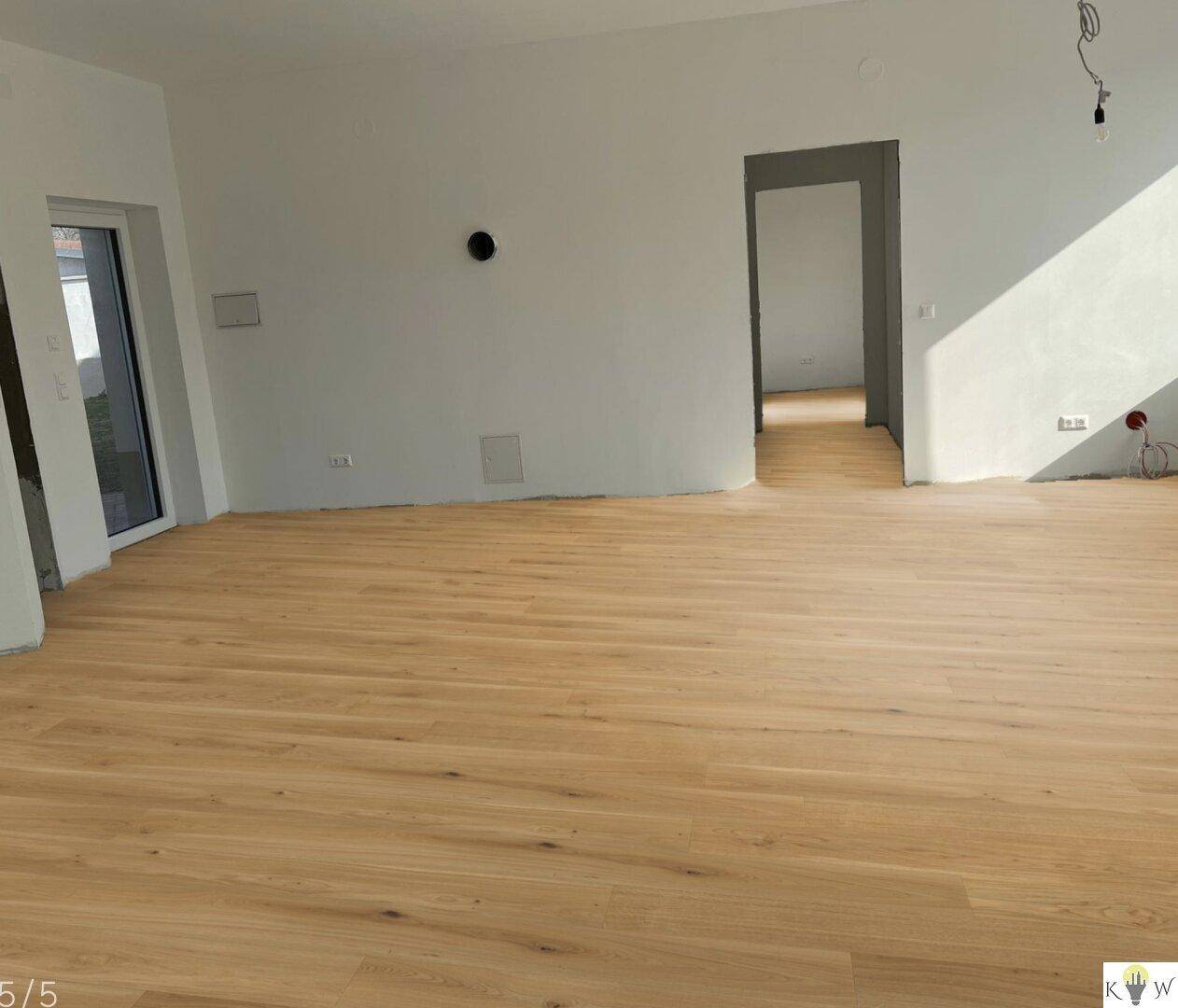 Geräumiger, heller Wohnbereich mit neu verlegtem Holzboden und Zugang zu weiteren Räumen.