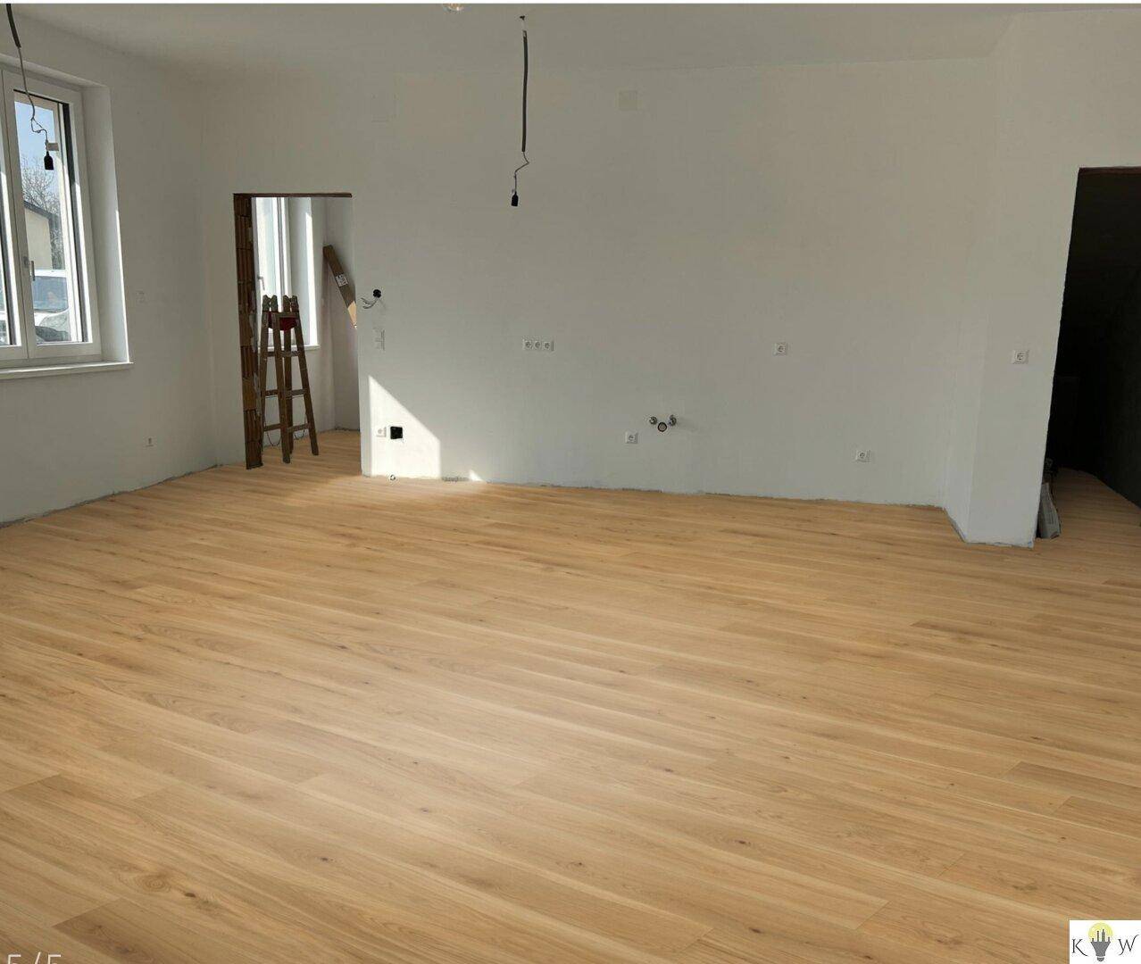 Lichtdurchfluteter Raum mit elegantem Holzfußboden und breiten Fensterfronten, frisch renoviert.