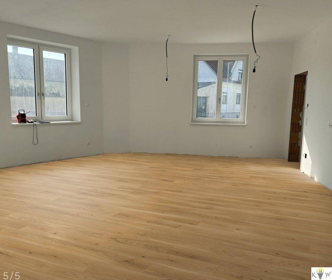 Heller, unmöblierter Raum mit neuem Holzfußboden und großen Fenstern, bereit zum Einzug.