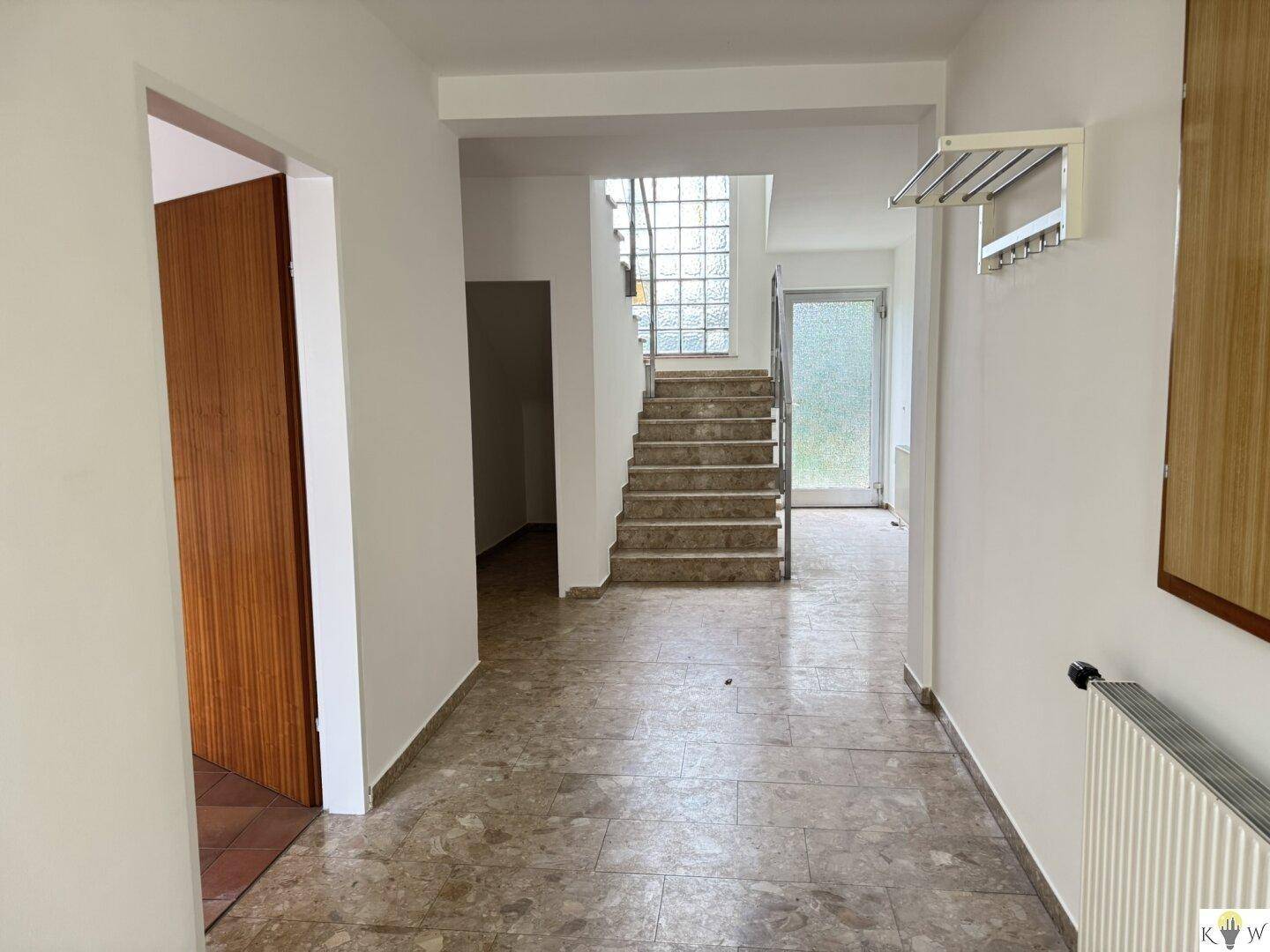 Heller Eingangsbereich mit Marmorfliesen, Treppe und dekorativer Glasbausteinwand.