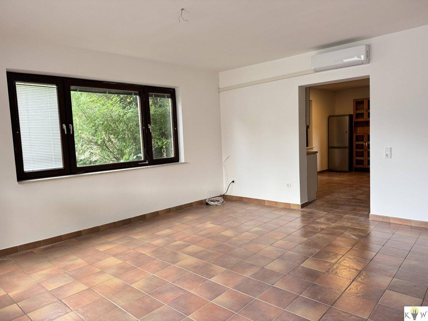 Heller Wohnbereich mit Terrakottafliesen, Klimaanlage und Zugang zur Küche.