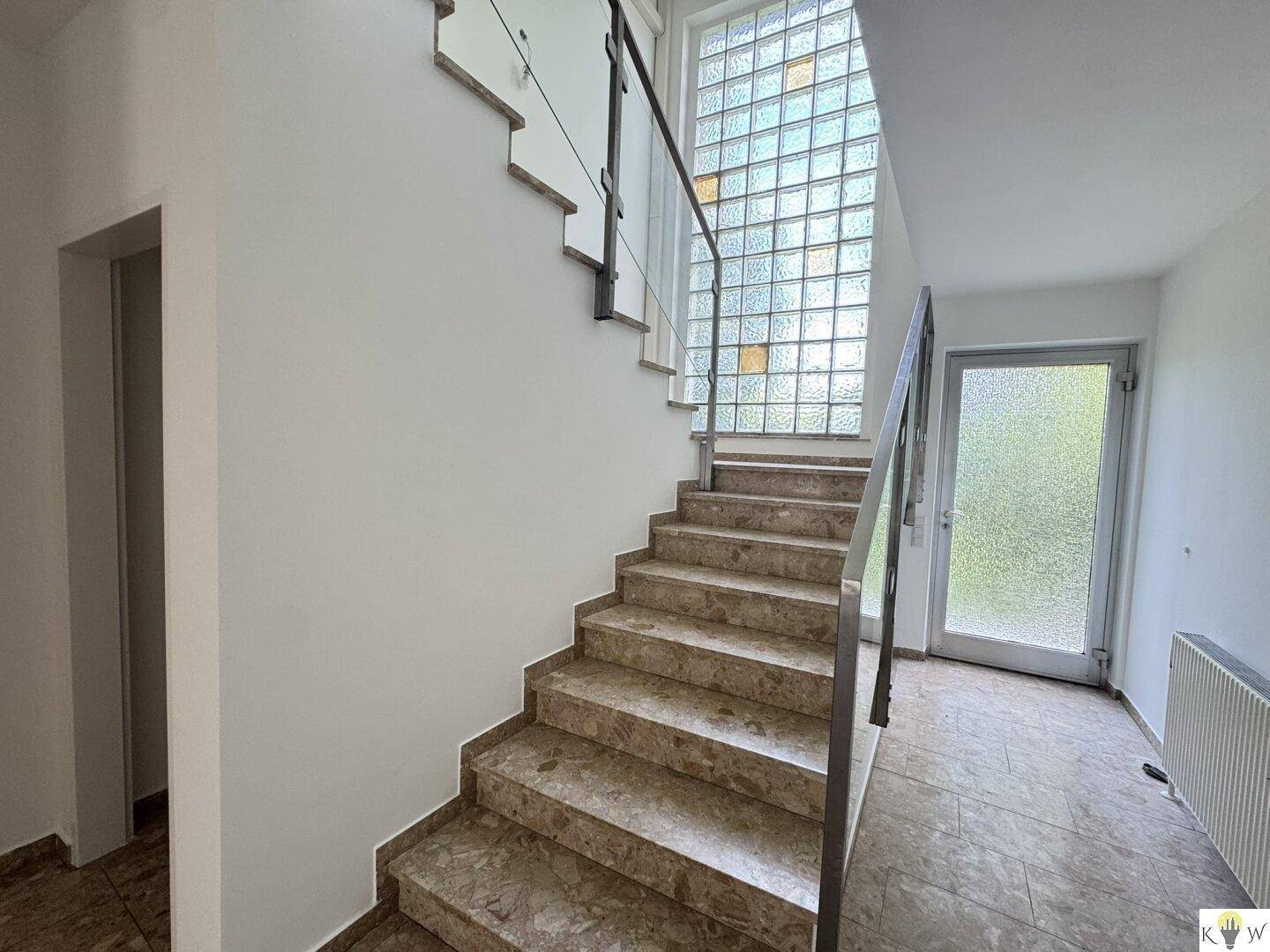 Treppenhaus mit Marmorstufen, Metallgeländer und Glasbausteinwand für natürliches Licht.