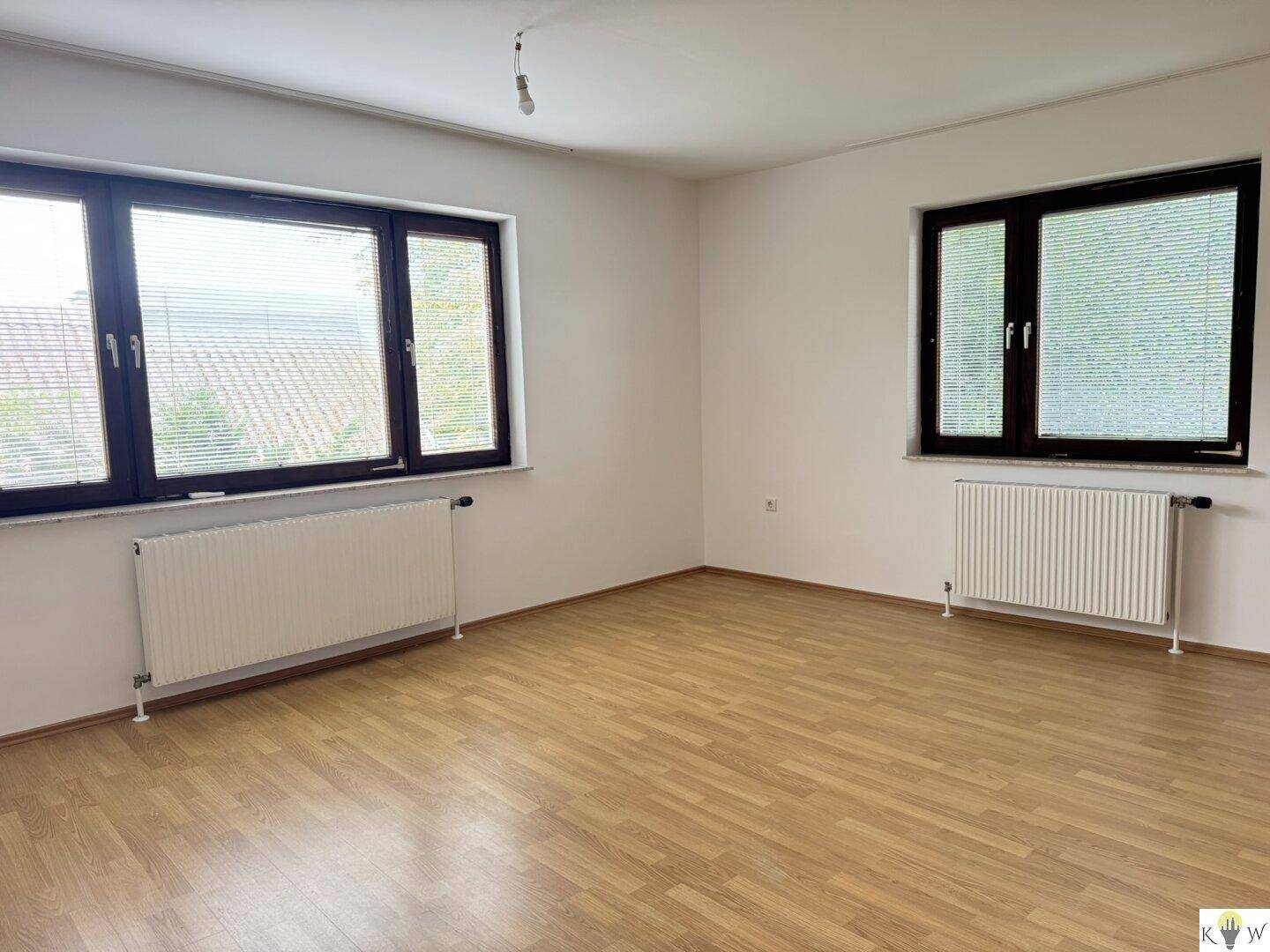 Schlafzimmer mit Laminatboden, Heizkörpern und zwei Fenstern mit Jalousien.