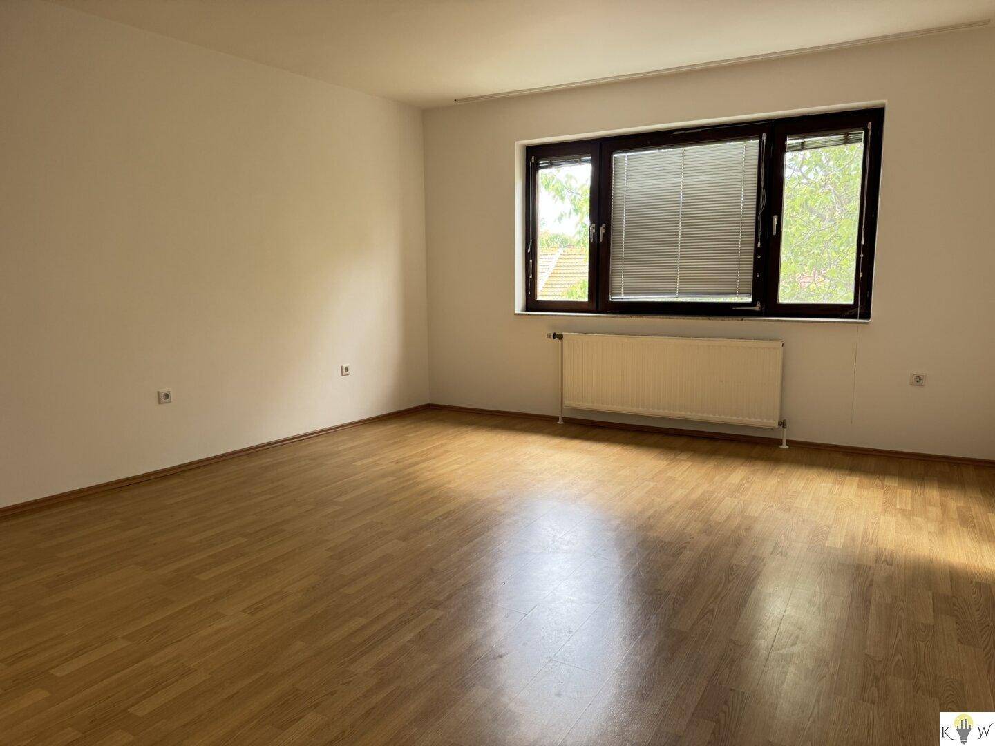 Geräumiges Schlafzimmer mit hellem Laminatboden, Heizkörper und großem Fenster.