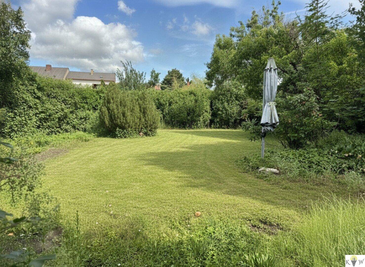 Großer, sonniger Garten mit Rasenfläche, umgeben von Hecken und Bäumen.