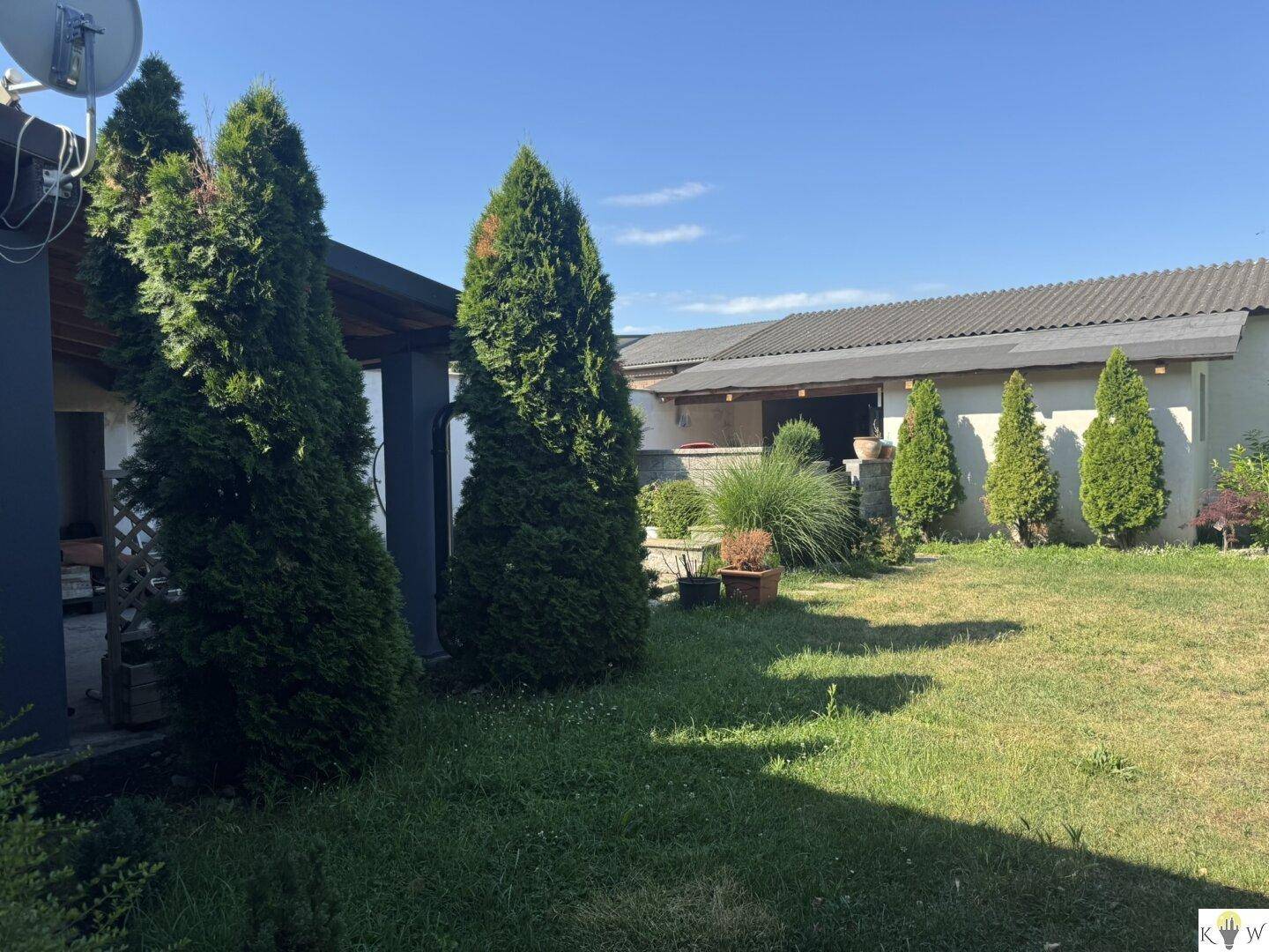 Gepflegter Gartenbereich mit Rasen, Bäumen und Sträuchern an einem sonnigen Tag.