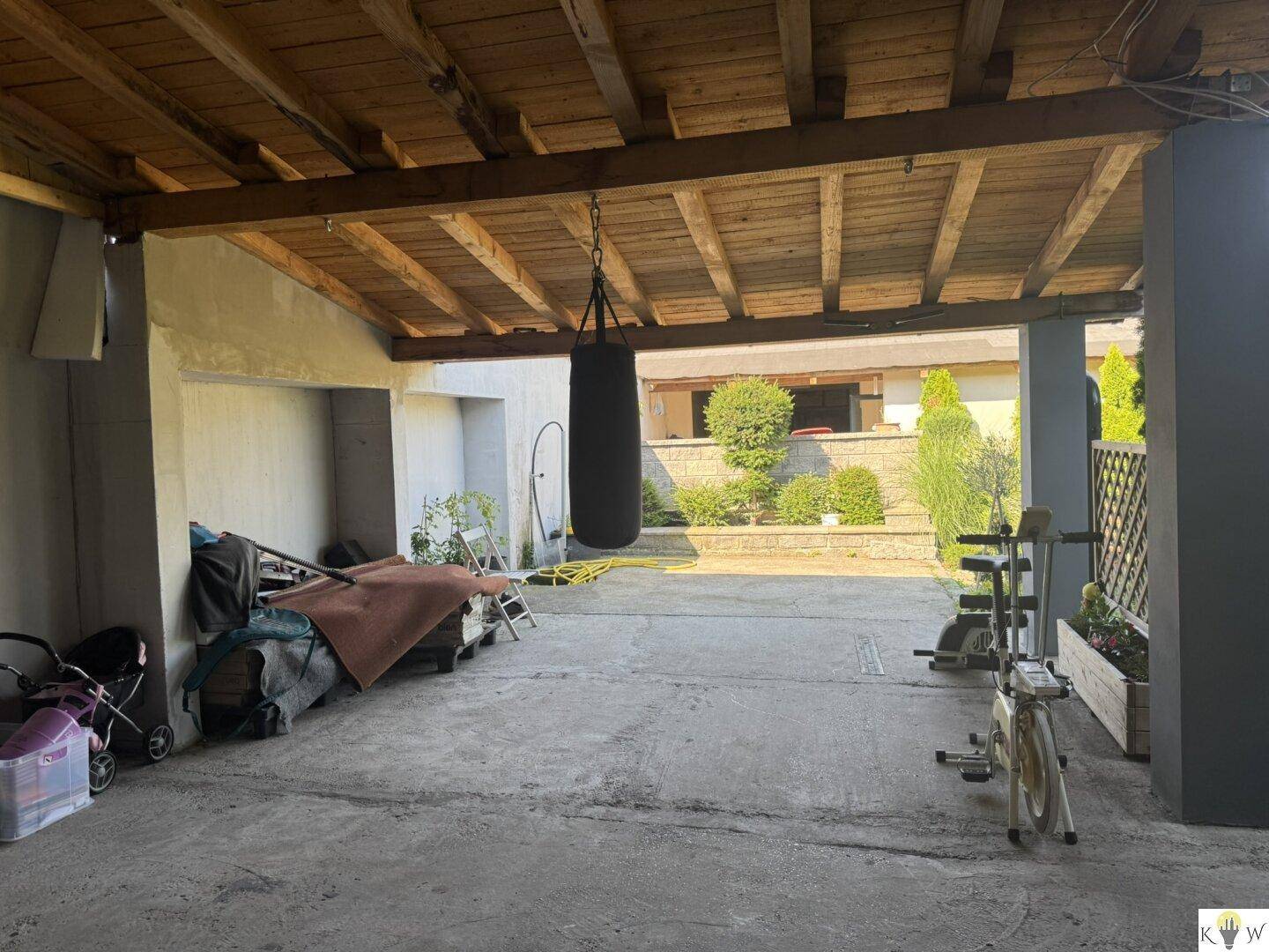 Überdachter Außenbereich mit Holzbalkendecke, Boxsack und Trainingsgerät.