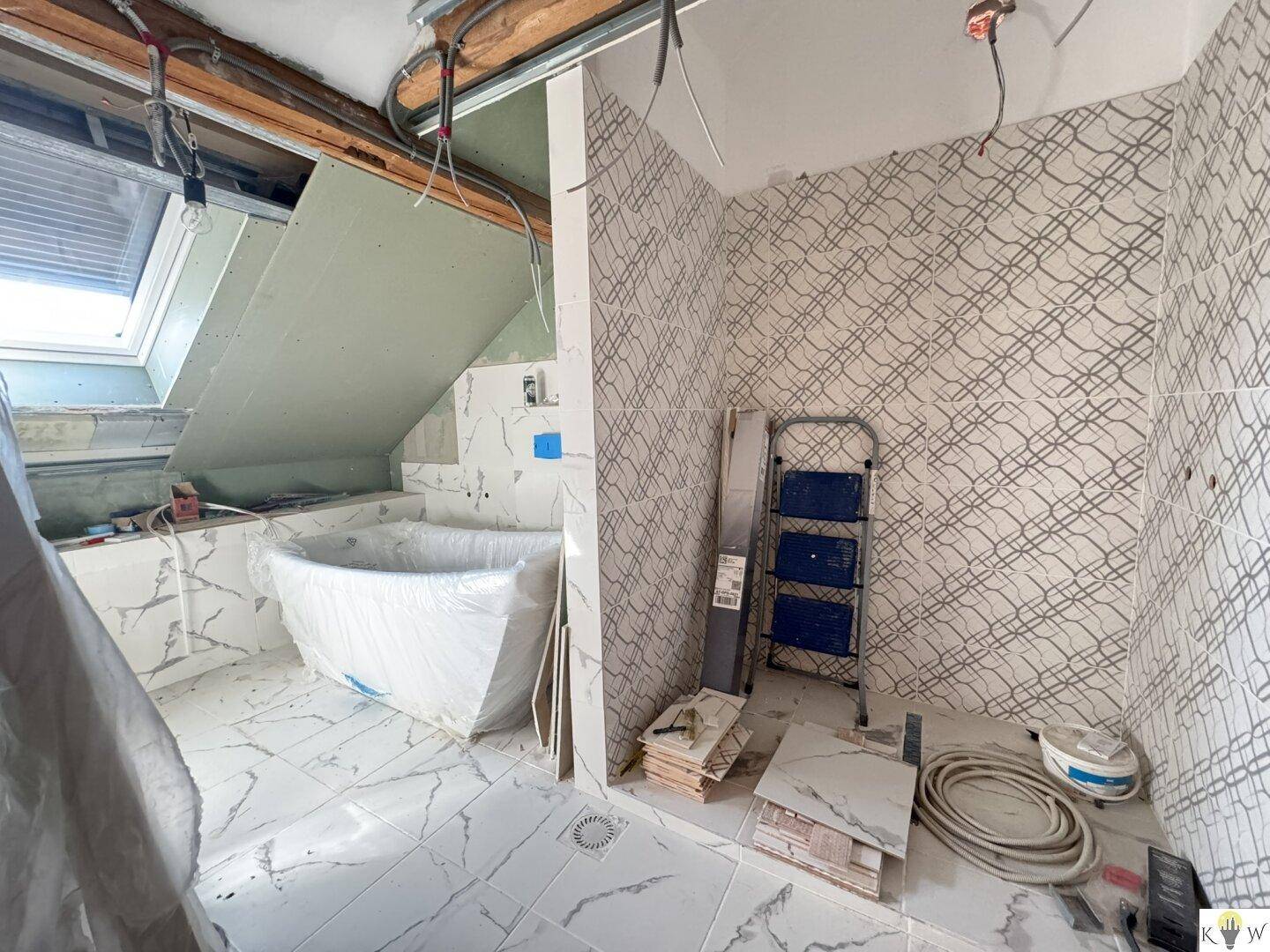 Badezimmer im Umbau mit Badewanne, Fliesen und sichtbaren Installationen unter einer Dachschräge.