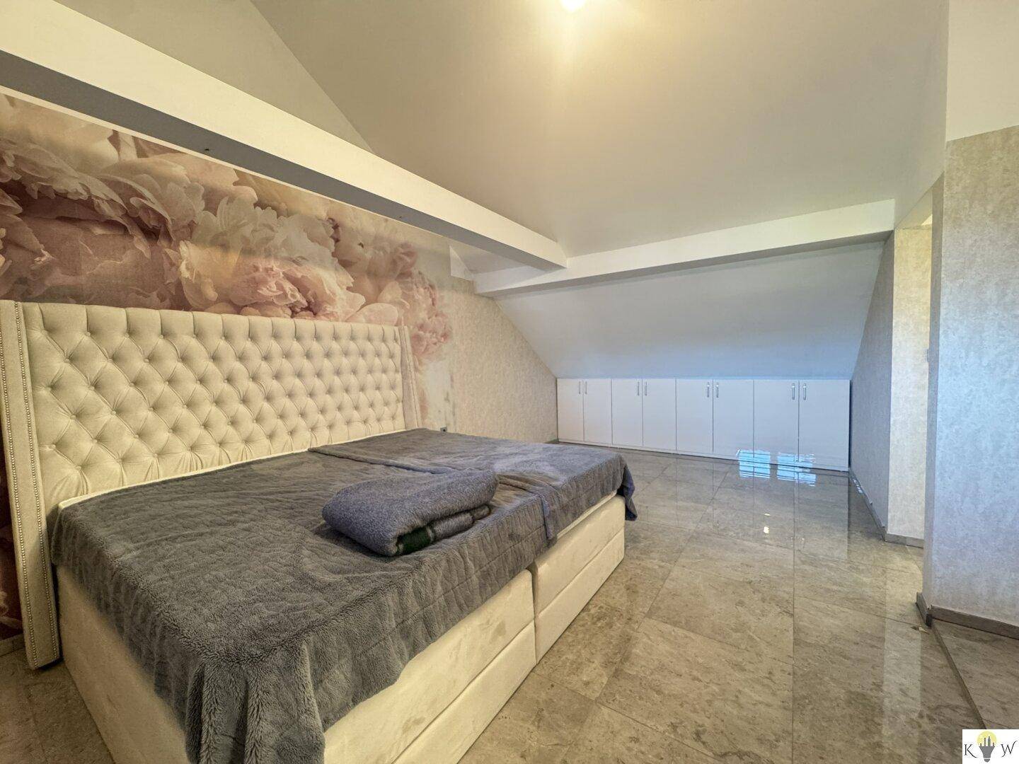 Dachgeschoss-Schlafzimmer mit großem Bett, Marmorfliesen und praktischen Einbauschränken unter der Schräge.