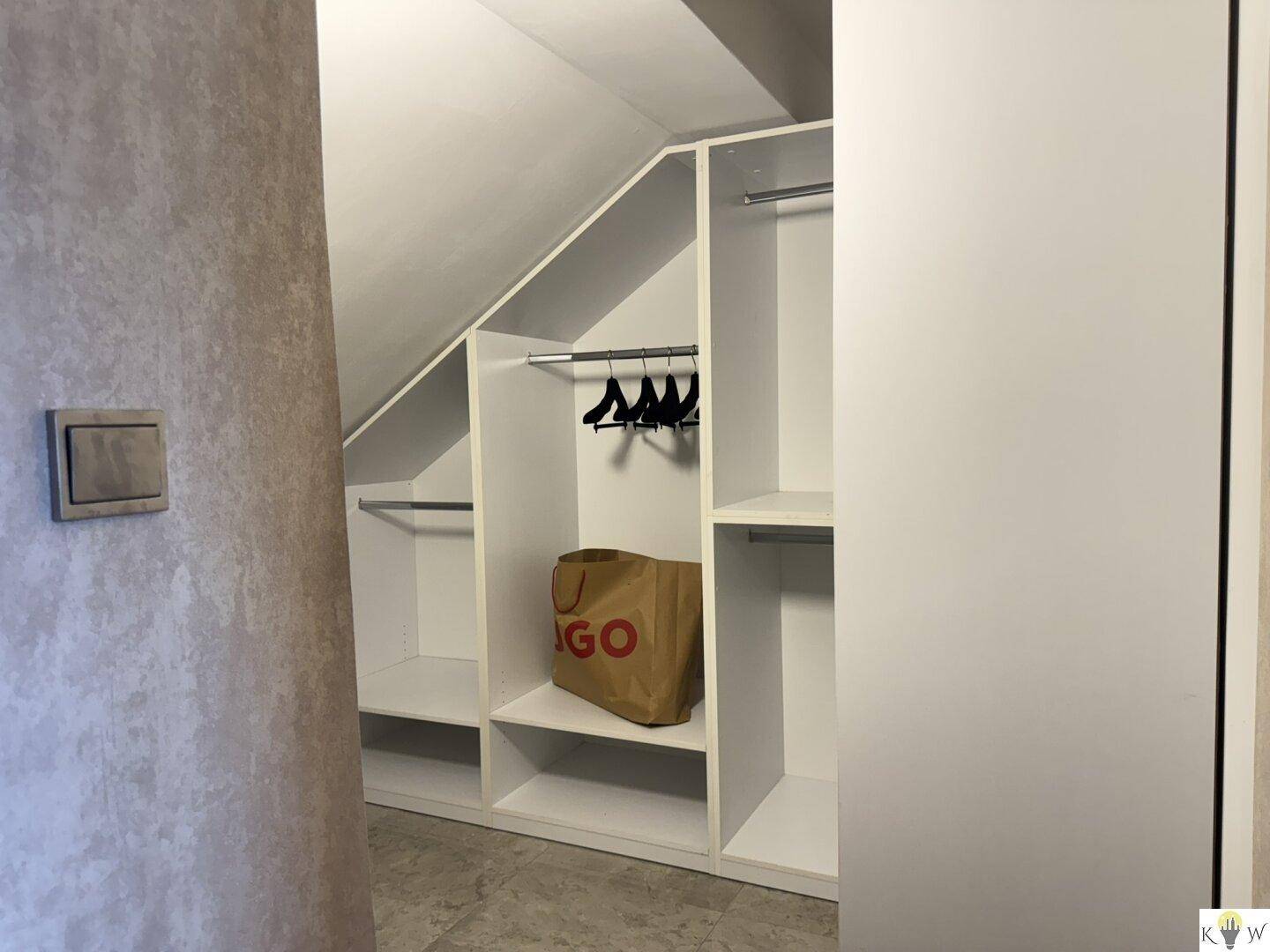 Begehbarer Kleiderschrank mit Regalen und Kleiderstangen unter einer Dachschräge.