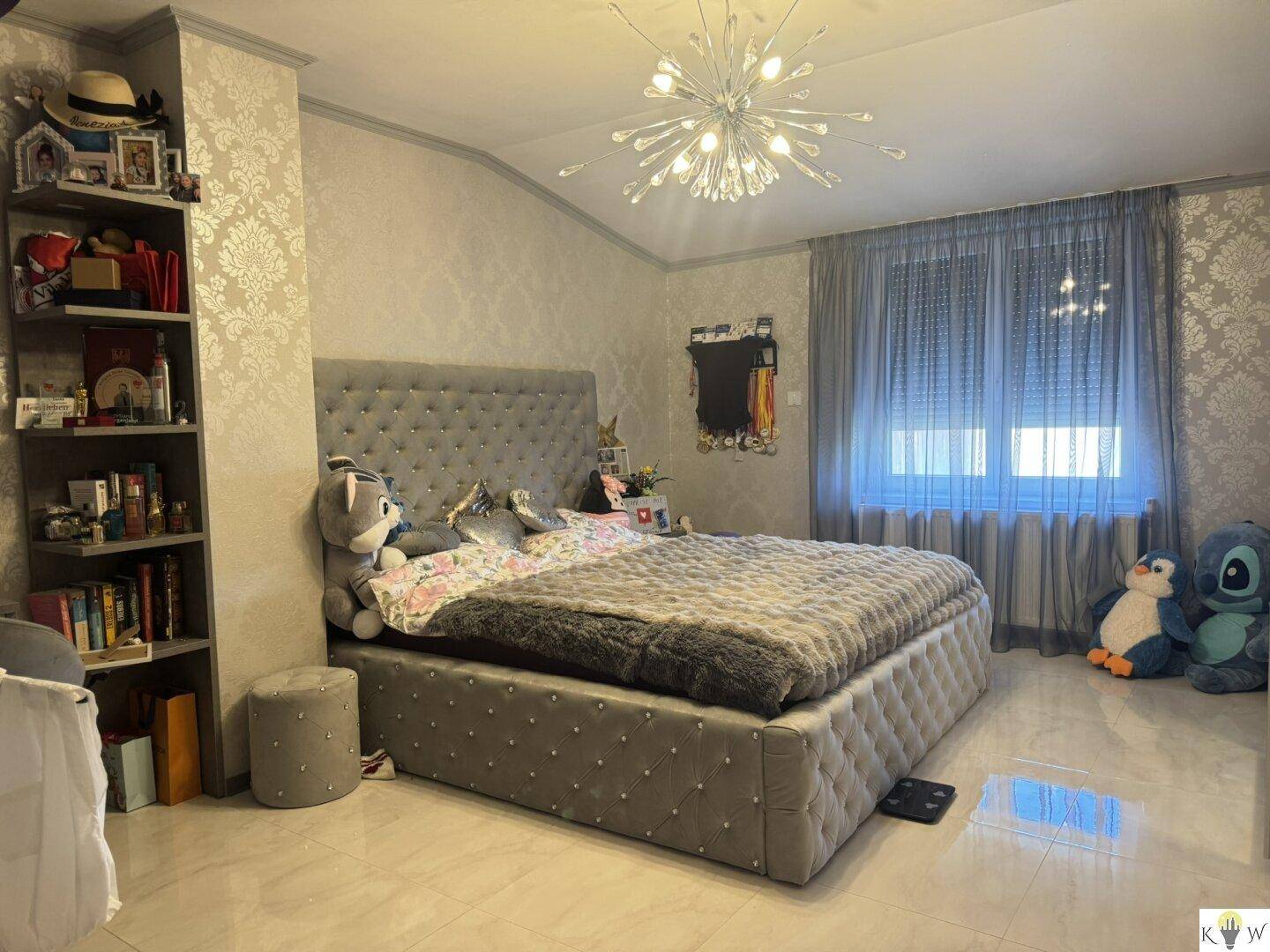 Elegantes Schlafzimmer mit großem Polsterbett, Fliesenboden und einem modernen Kronleuchter.